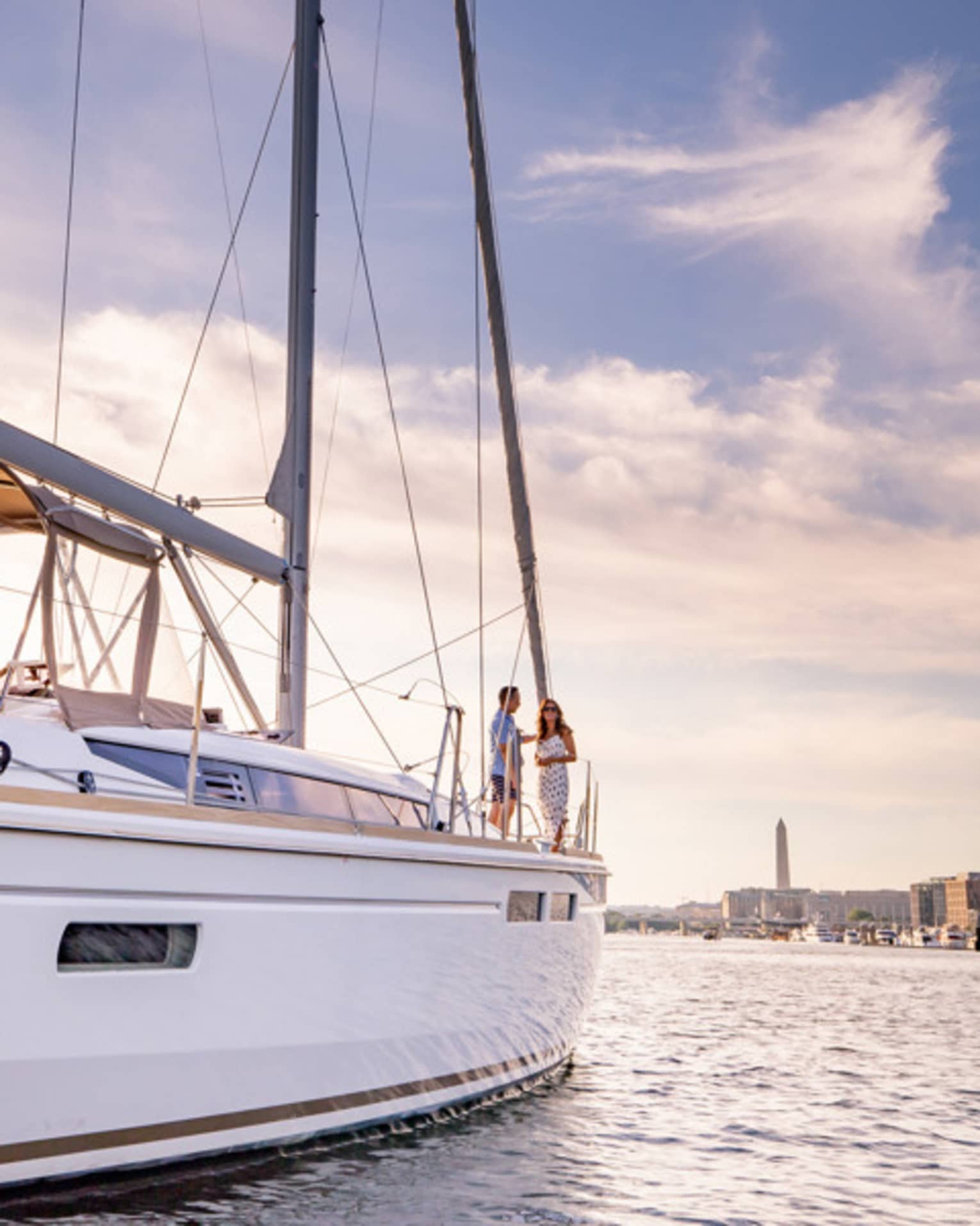 Two guests standing on a boat in the water with a view of the city in the background.