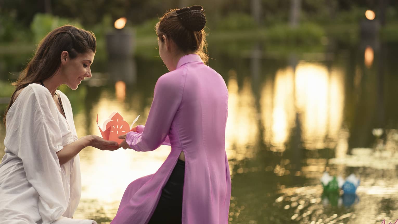 Two women prepare to release paper boat with love letter onto lotus pond