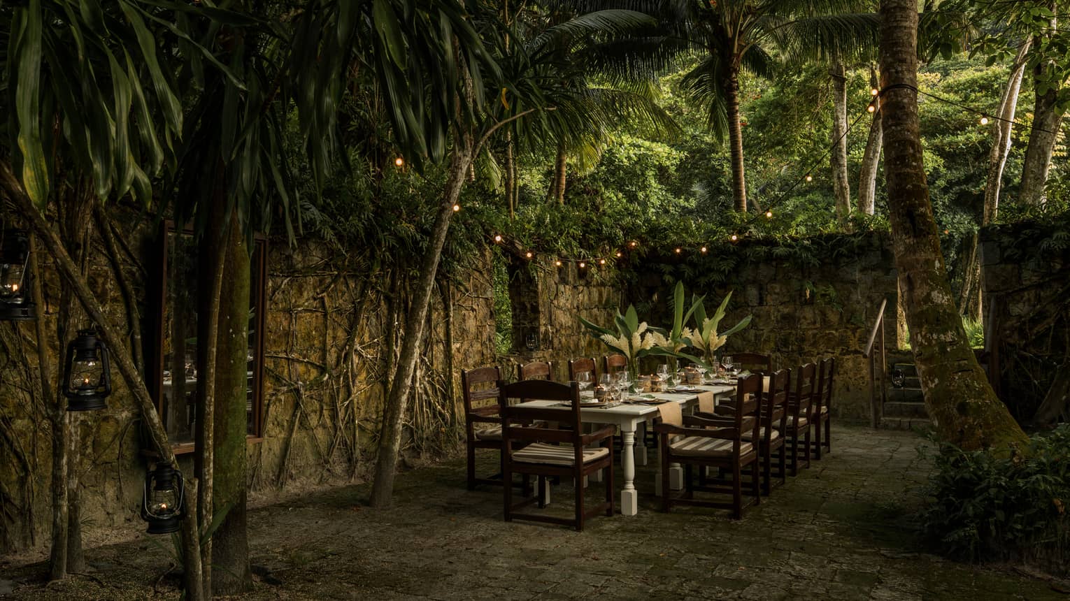 Long dining table with chairs outdoor under palm leaves, near the Foumba Creole ruins at Kannel restaurant