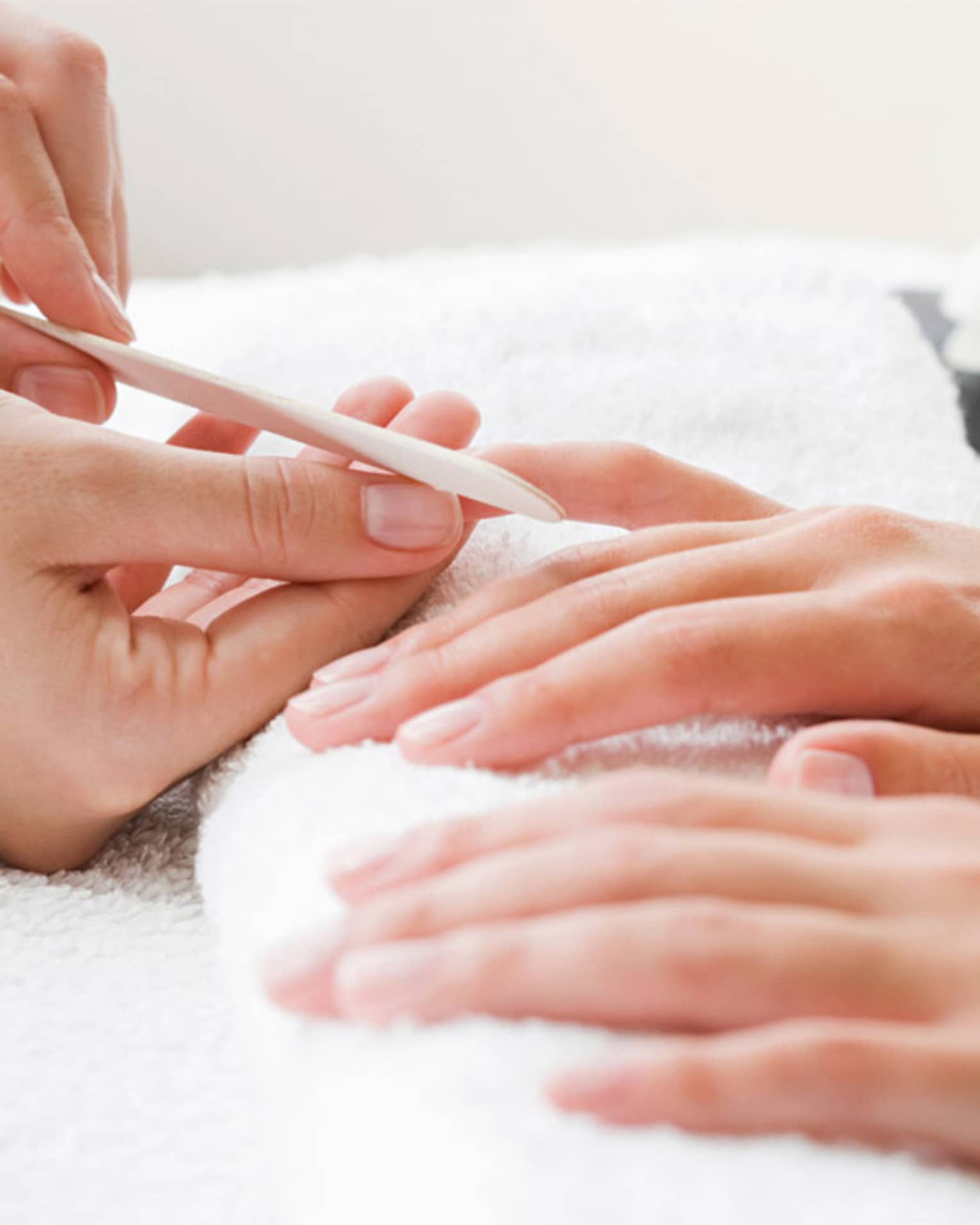 Close-up of spa attendant filing nails of woman's hands as they rest on white towel