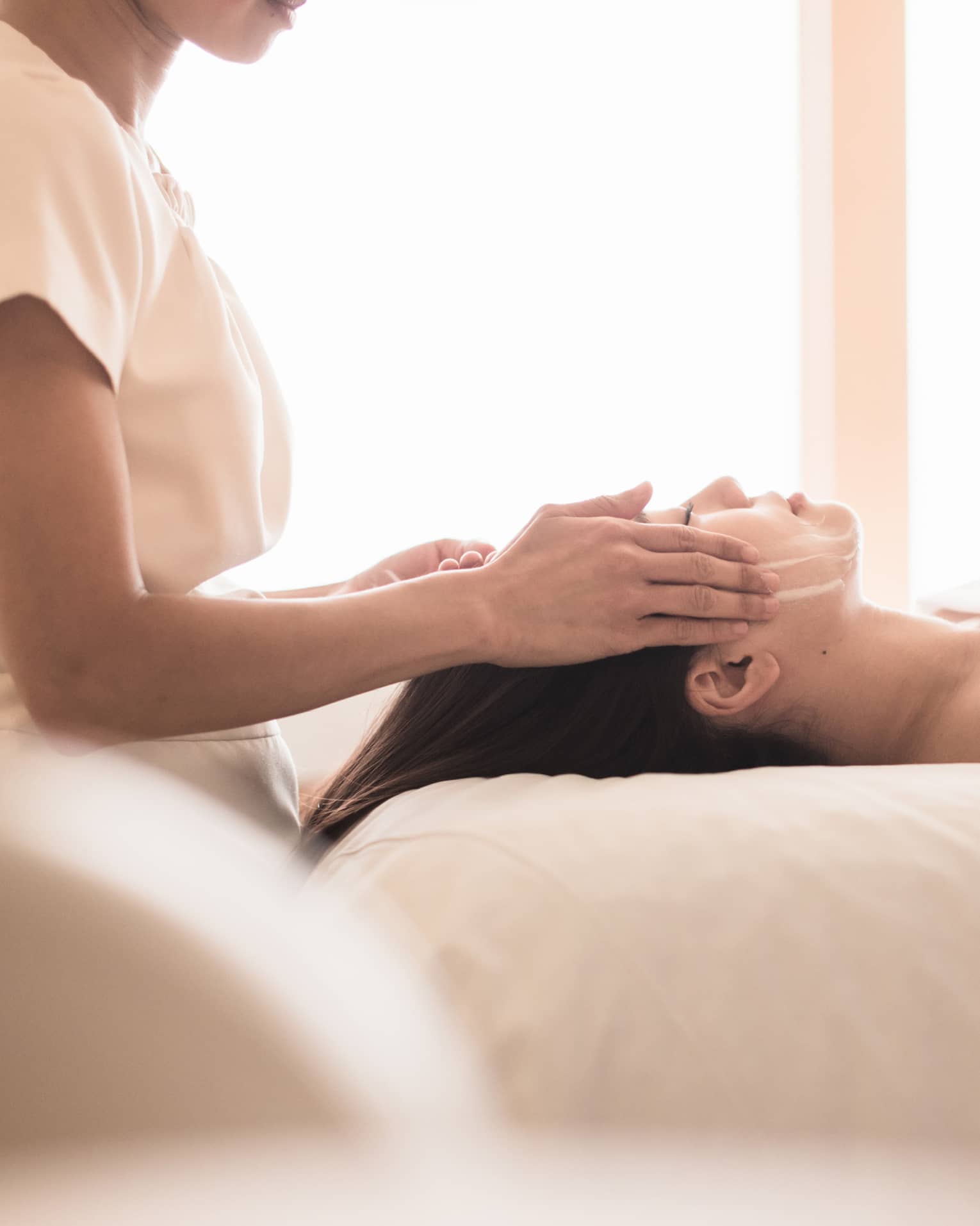 Spa staff massages woman's forehead, temples as she lies on massage table