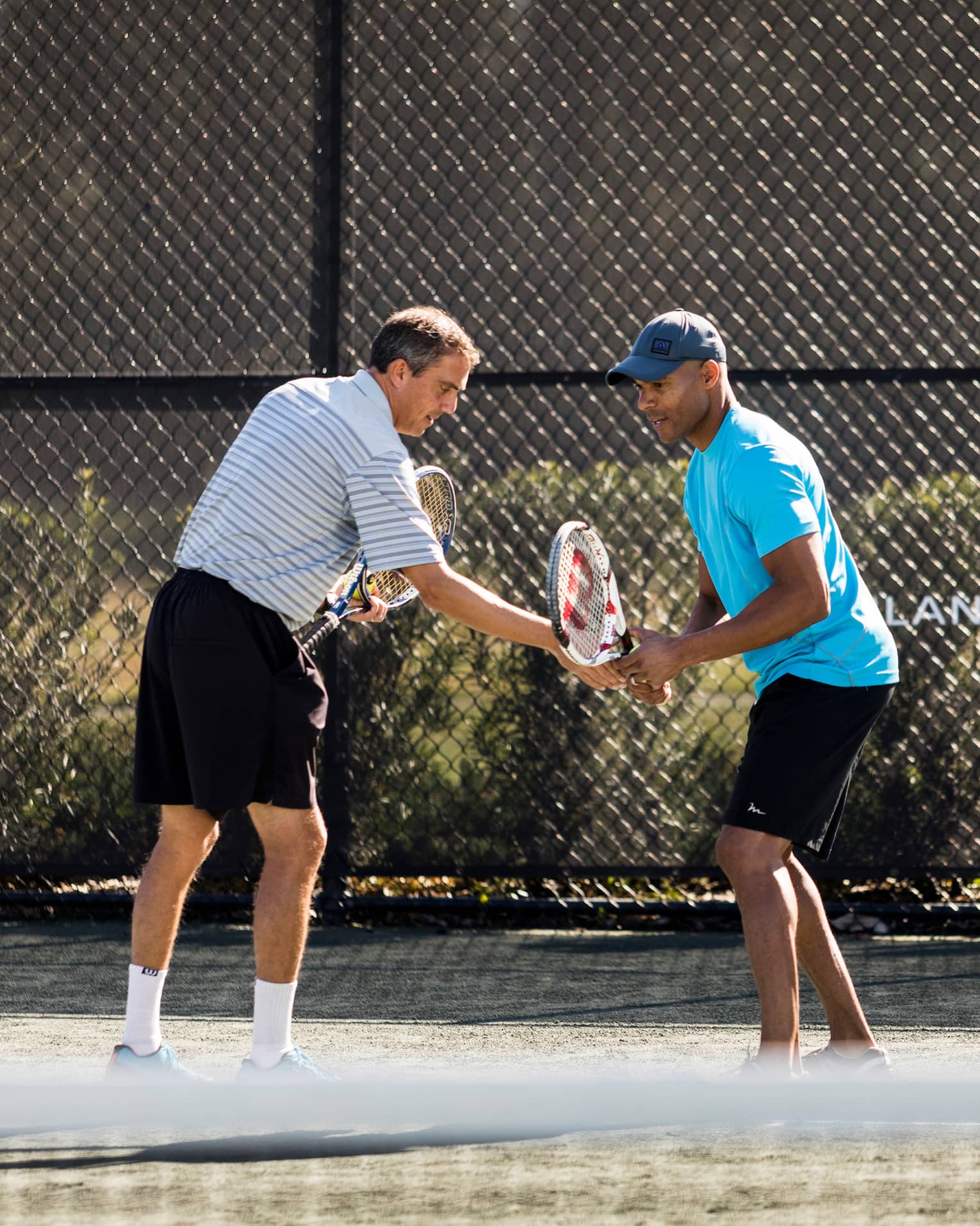 Tennis pro helps man adjust his racket on tennis court by Four Seasons Resort logo on fence