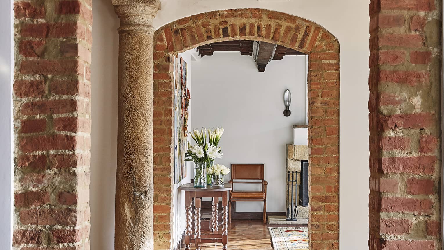 Rustic brick archways, pillars, lead to bright hotel room with wood table with fresh white flowers