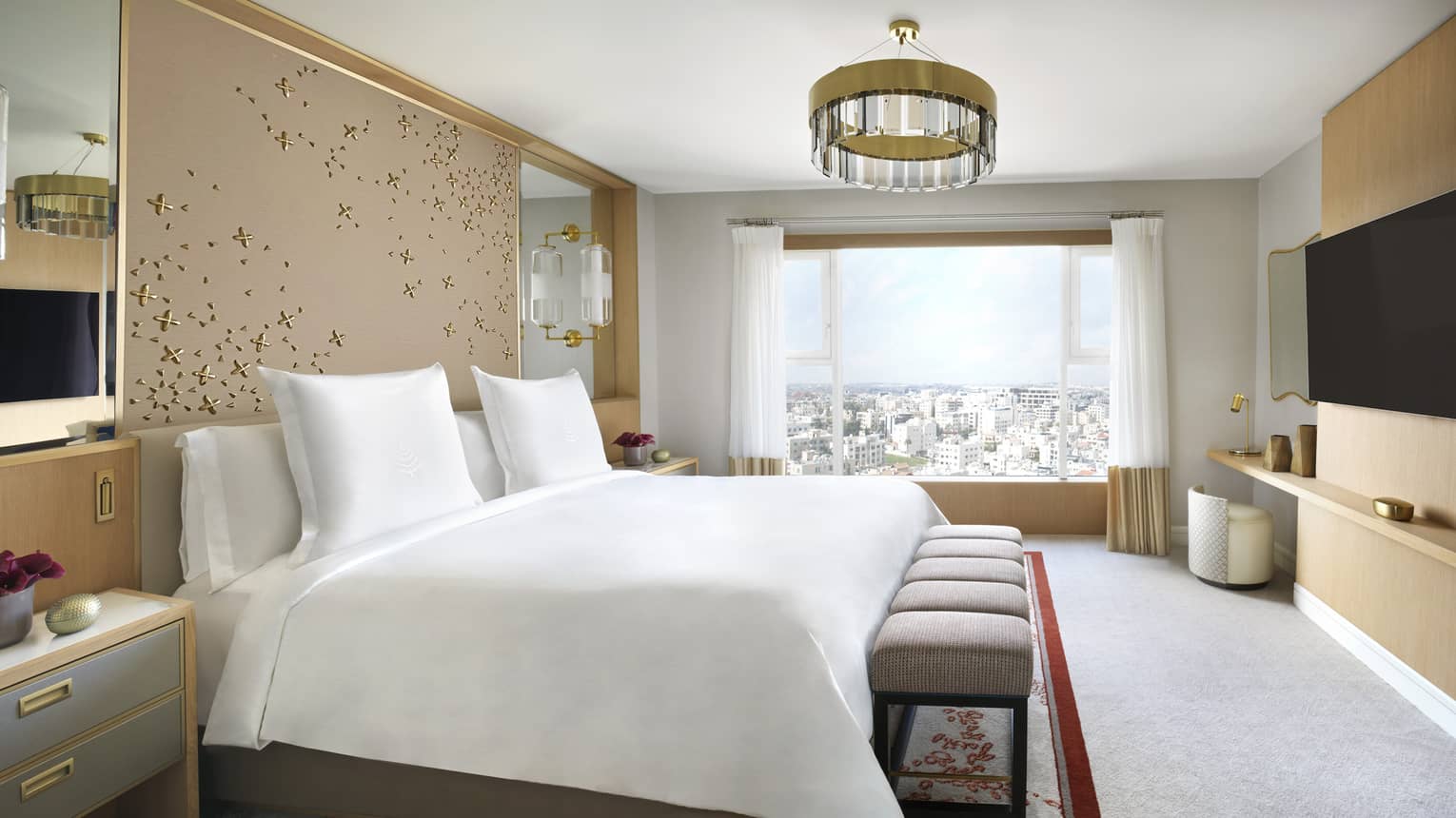 A floral decorated room with a large white bed in the centre, and a cityscape view. 