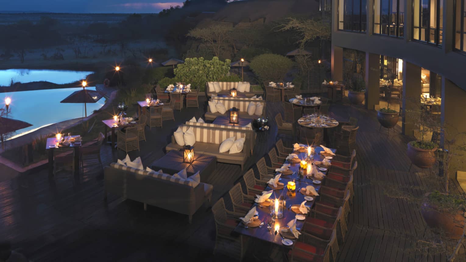 Glowing candles on patio dining tables near blue outdoor swimming pool, sky