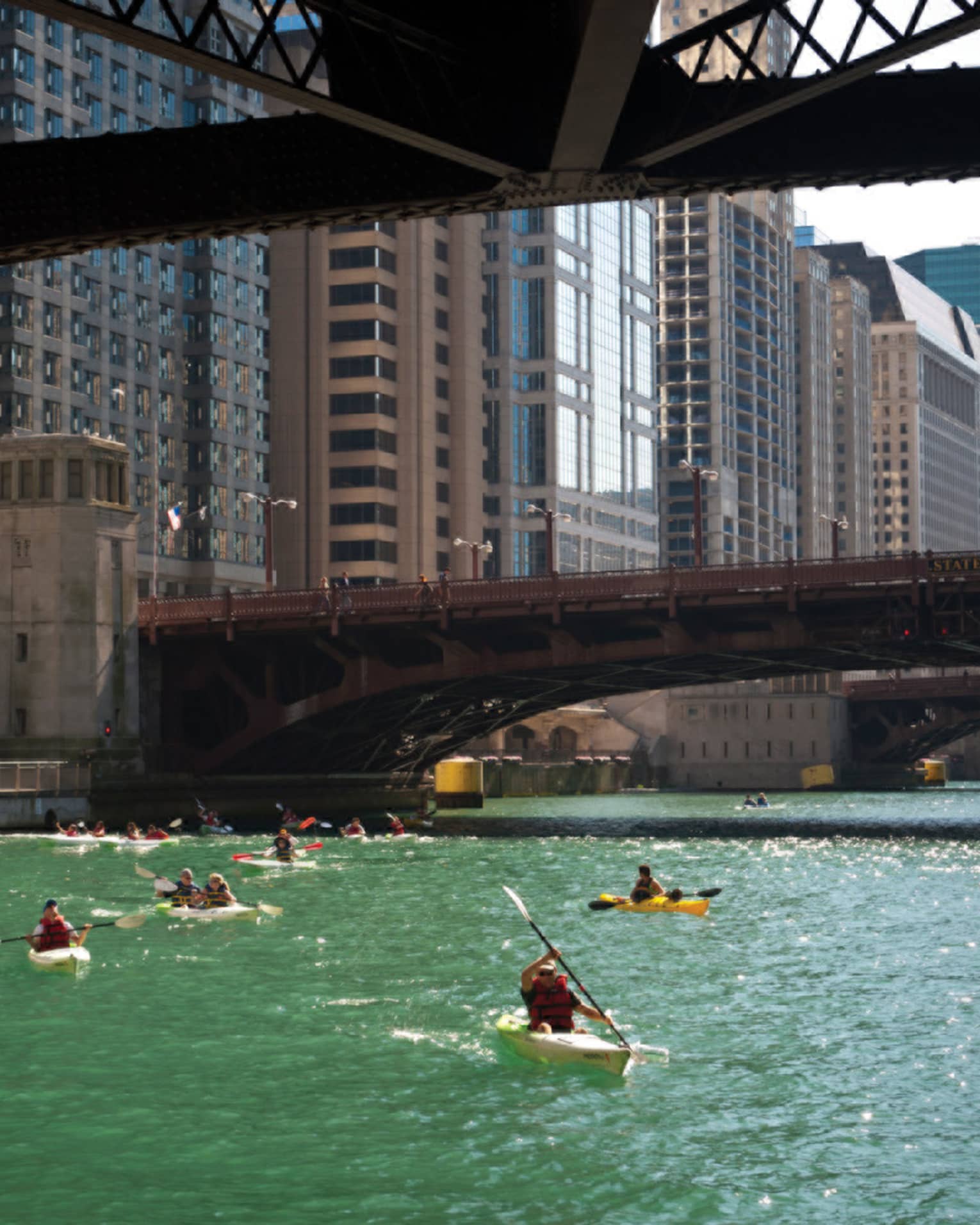 People kayaking on a river under a bridge.