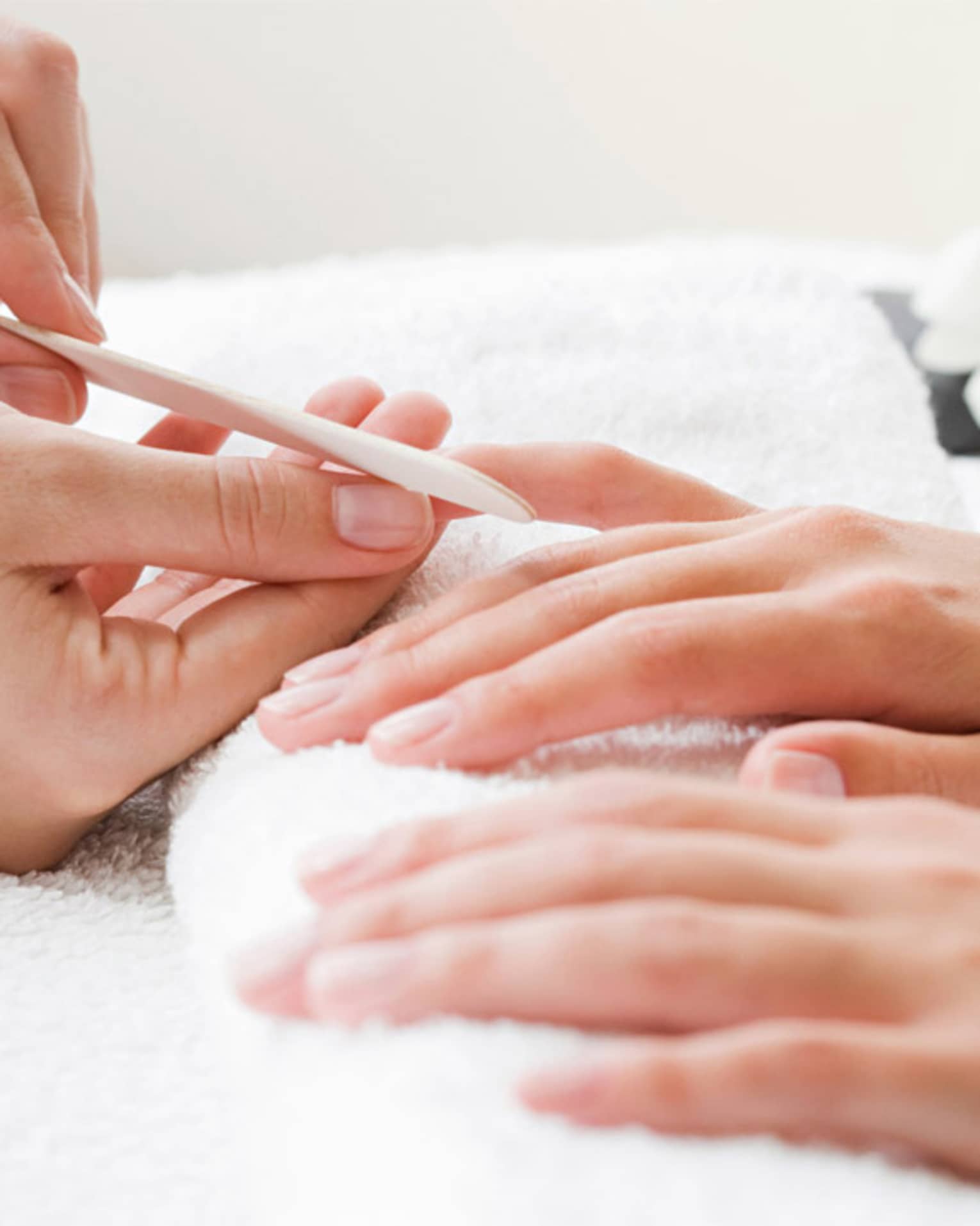 Close-up of spa attendant filing nails of woman's hands as they rest on white towel