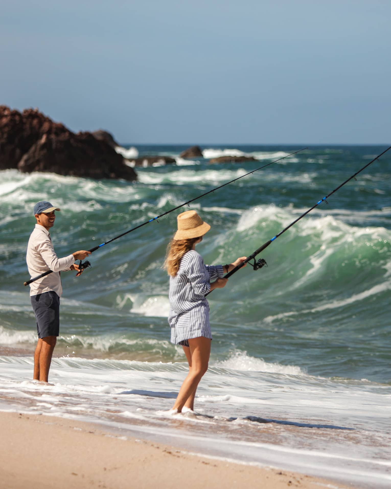 Two people fishing on a beach shore.