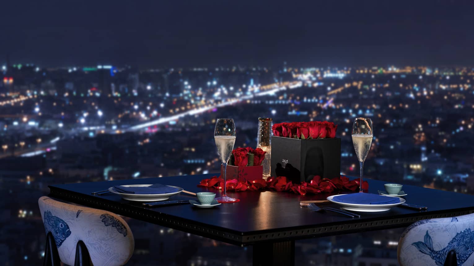 Sintoho dining table, red roses and Champagne glasses by window overlooking city lights below