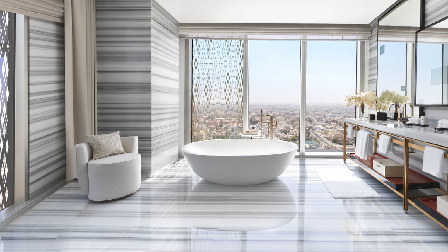 Large Royal Suite bathroom with modern striped marble floors, walls, freestanding tub, armchair