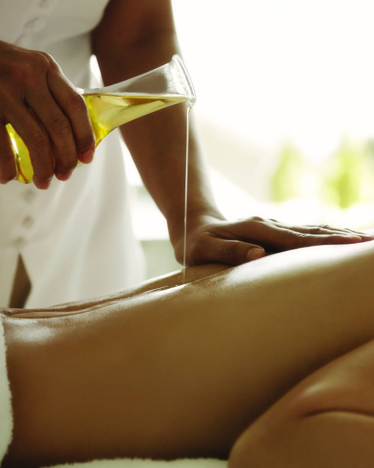 Spa staff pours massage oil over woman's bare back as she lays on treatment bed