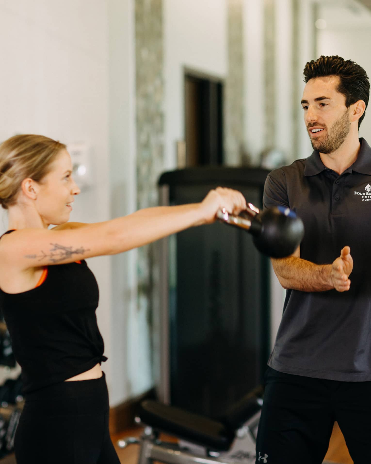 Male fitness trainer works with female guest who is using a kettlebell