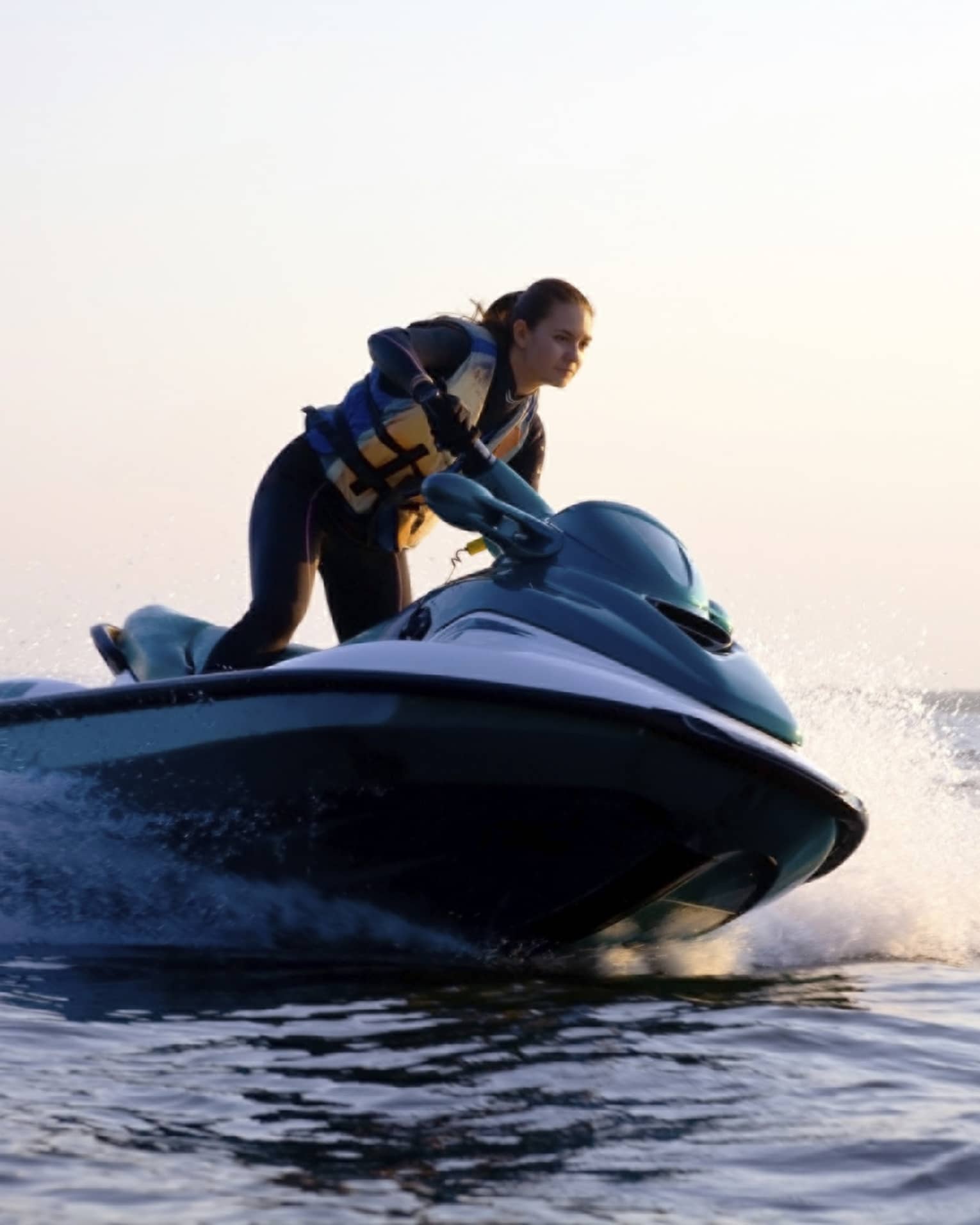 Woman wearing life jacket stands, steers jet ski on ocean at sunset