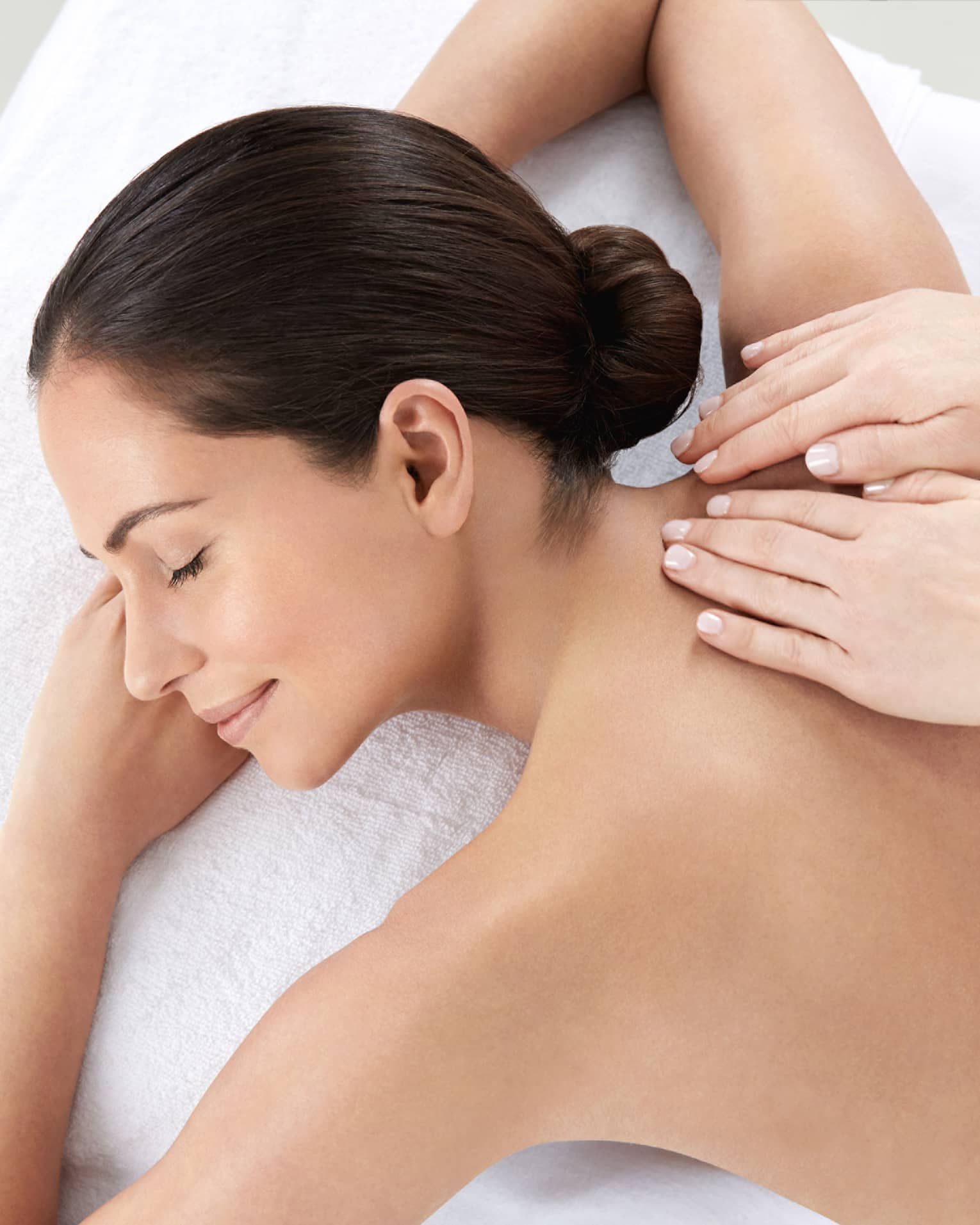 Woman smiles, lies on massage table as hands massage bare shoulders