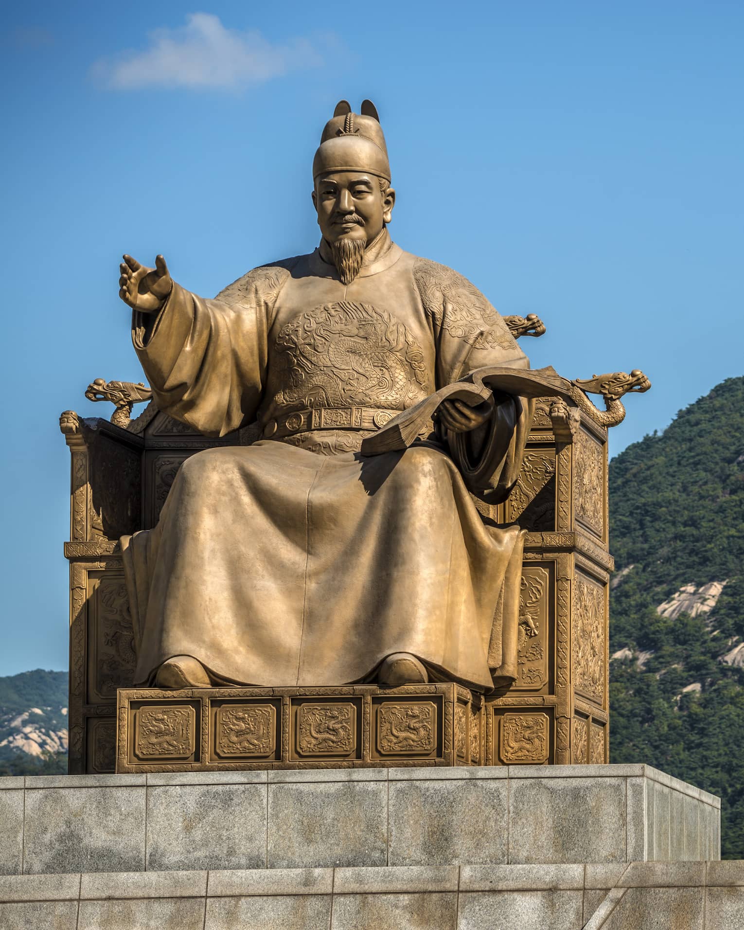 Golden statue of Sejong the Great, cloudless blue sky, lush green mountains in the background