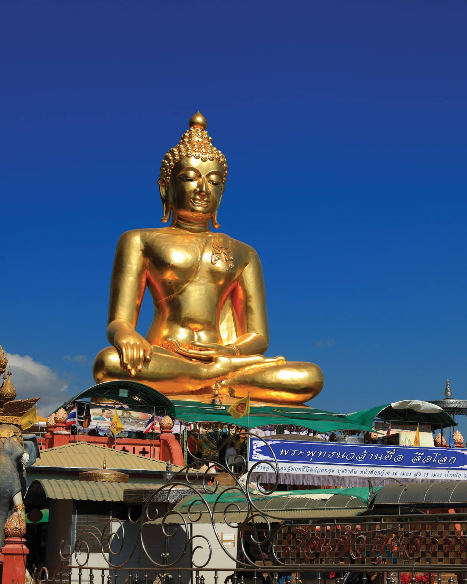 Gold Buddha statue on temple roof against a blue sky