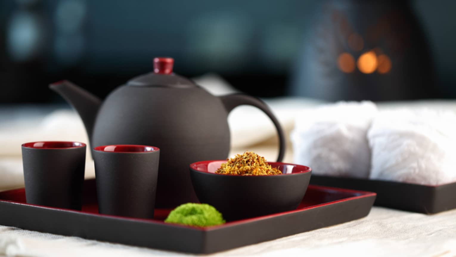 Black-and-red modern teapot with two mugs and bowl of loose-leaf chamomile on serving tray