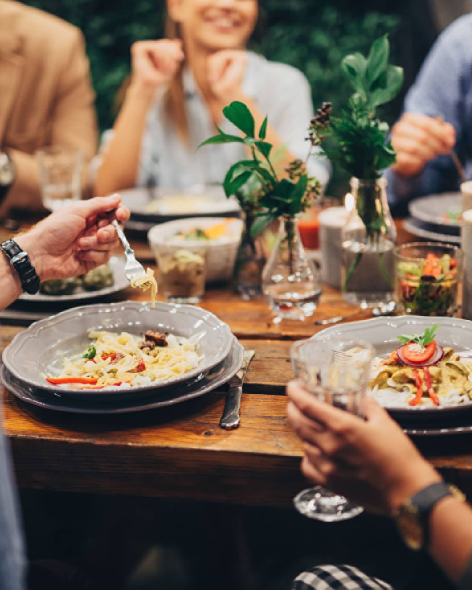 Close-up of group of friends around gourmet pasta dishes on outdoor table