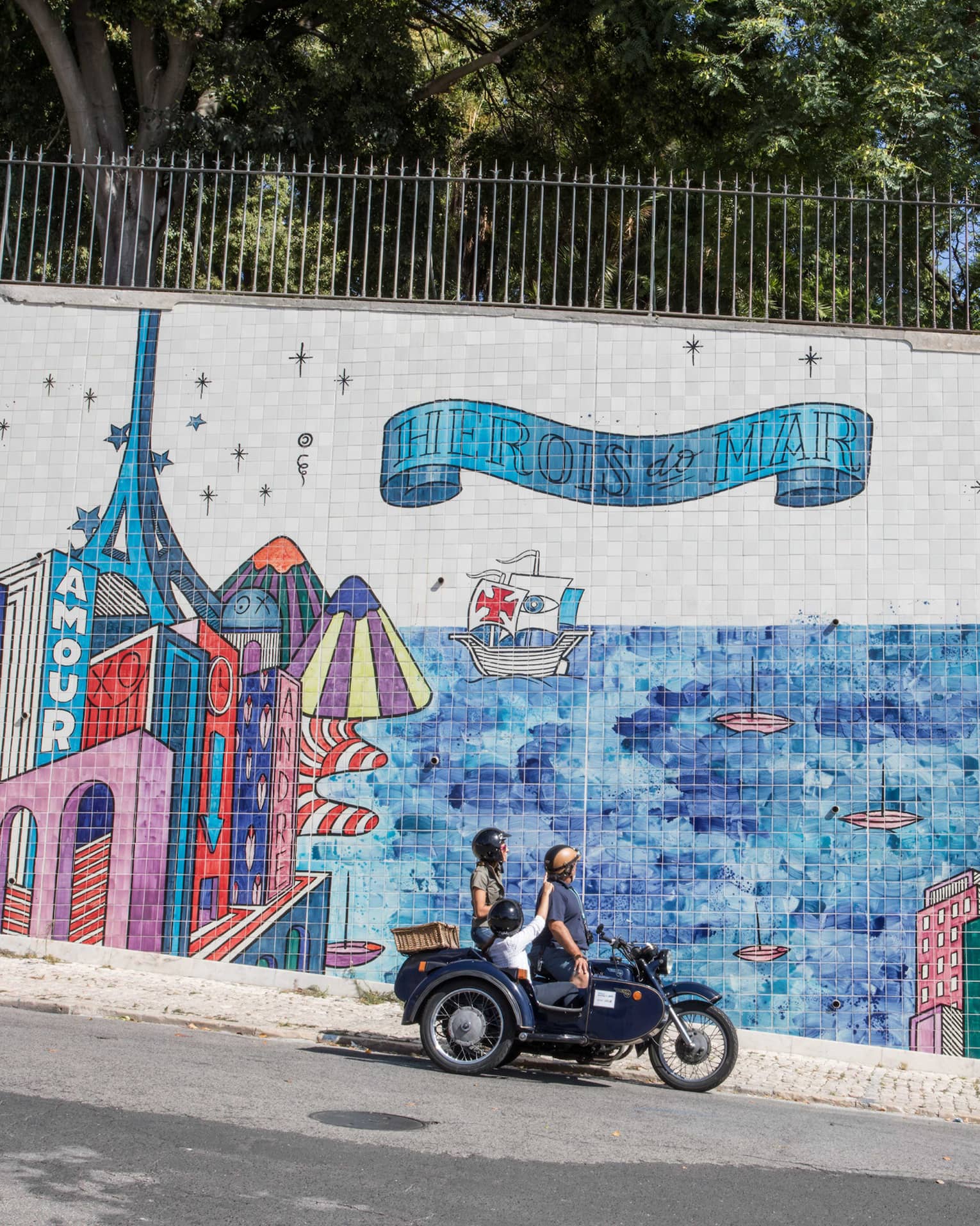 Two adults and a child stop their motorcycle to look at a city mural made of tiles