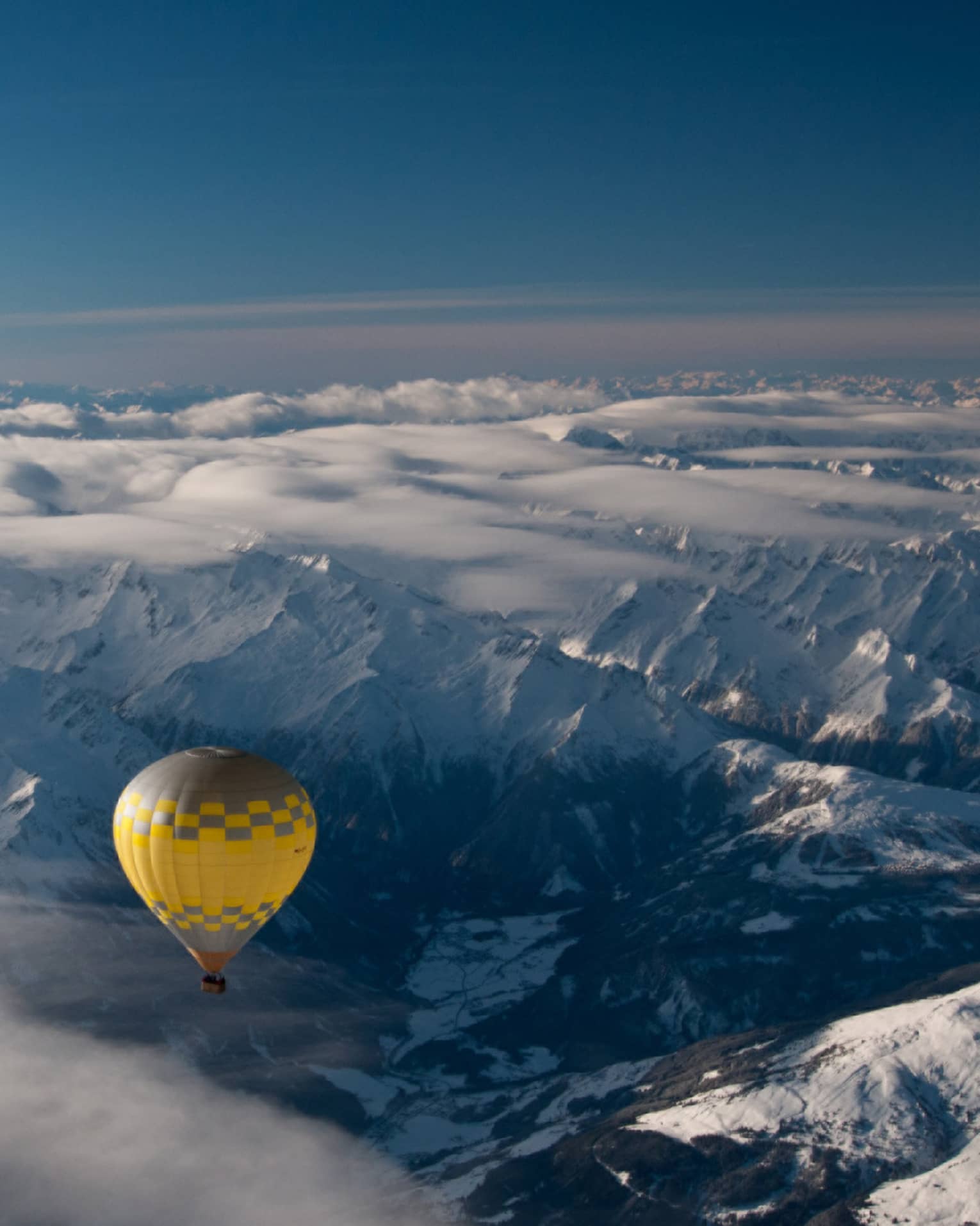 Yellow hot air balloon soaring over the snow-covered Alps