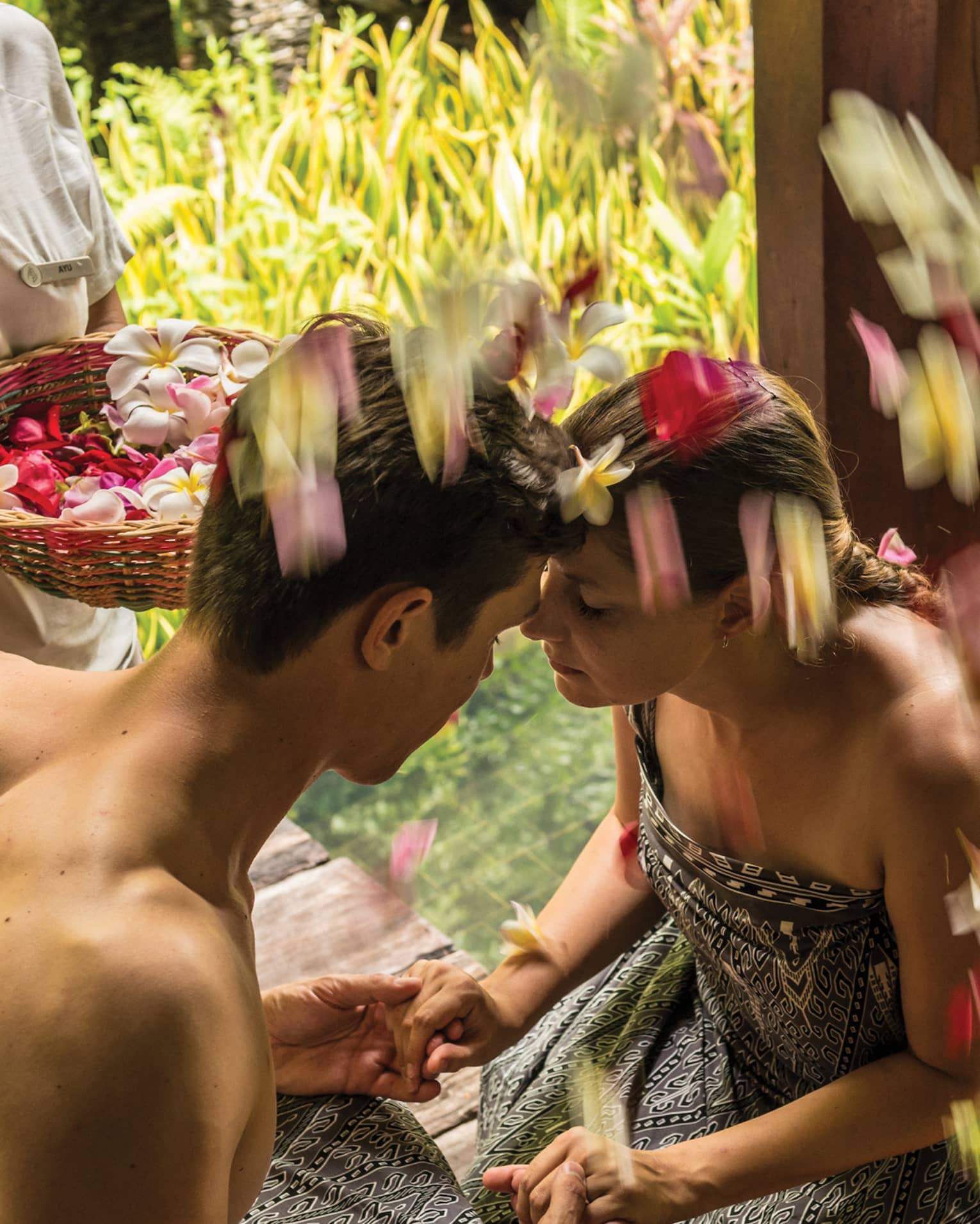 Couple on chairs, hold hands, foreheads together as woman sprinkles flower petals