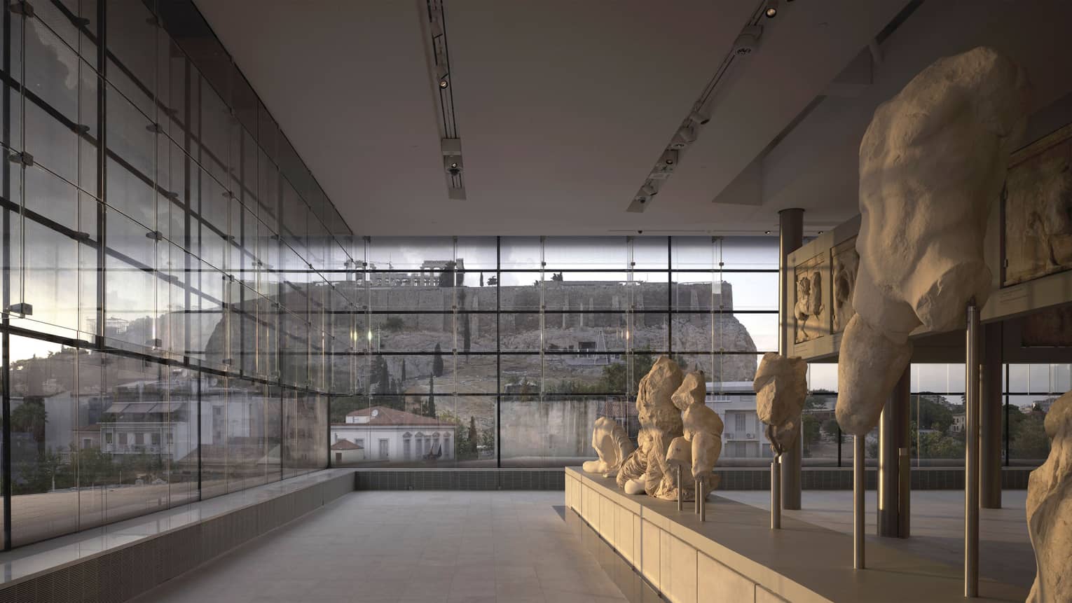 Greek sculptures on display in glass room overlooking ruins at Acropolis Museum