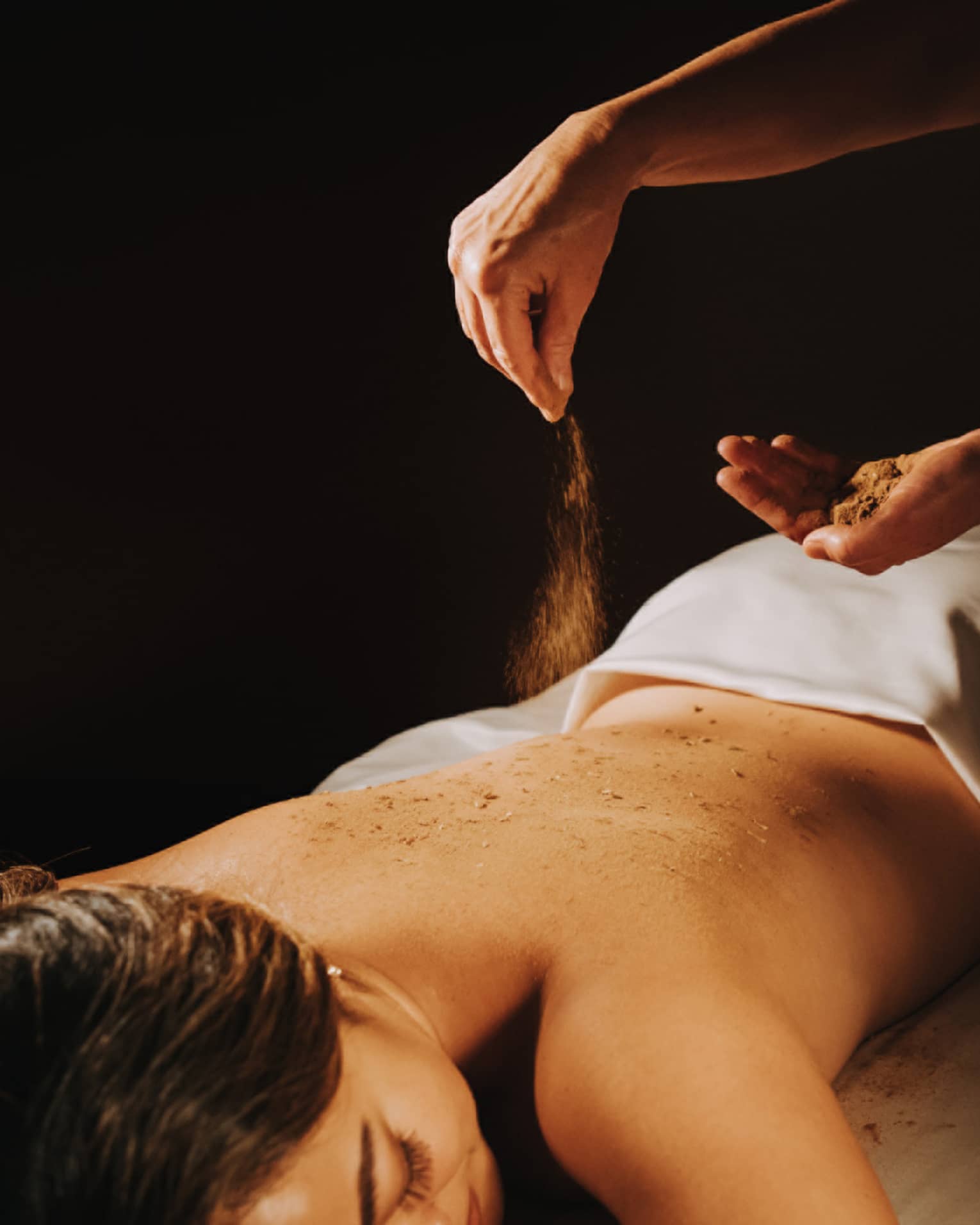 Spa staff sprinkled coffee powder over woman's bare back as she lays on massage table