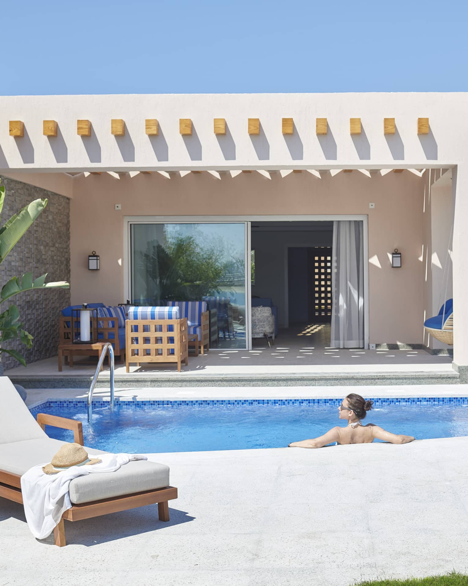 Female guest lounges in private pool at her beach villa, blue skies overhead