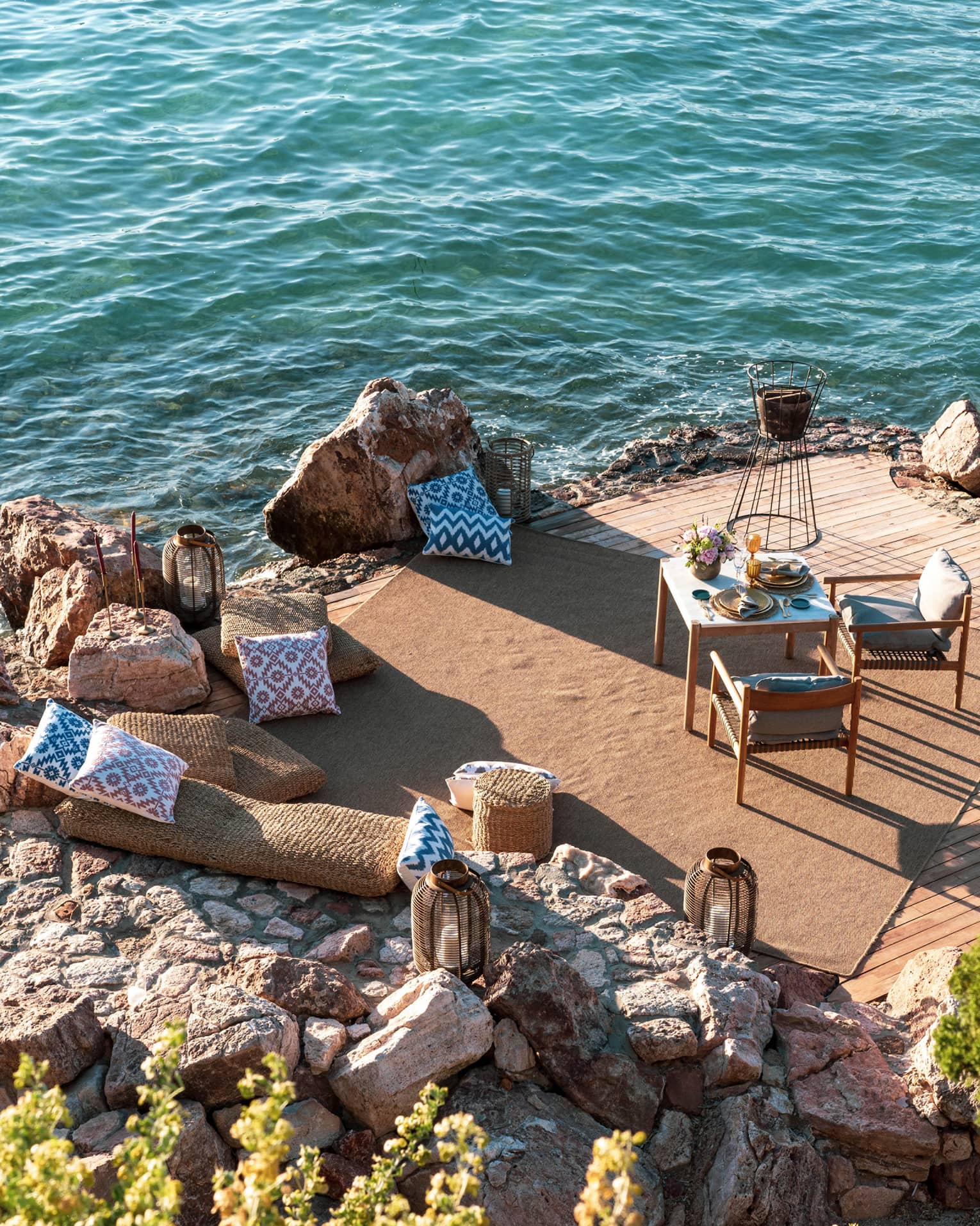 A dining table with two chairs is set on a private rocky peninsula next to the sea