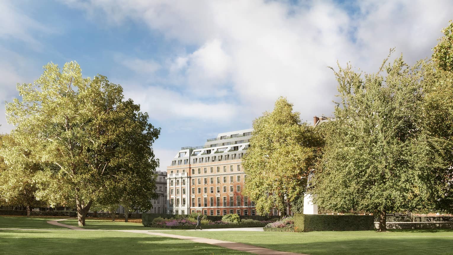 View across long green park, path between trees to building in background