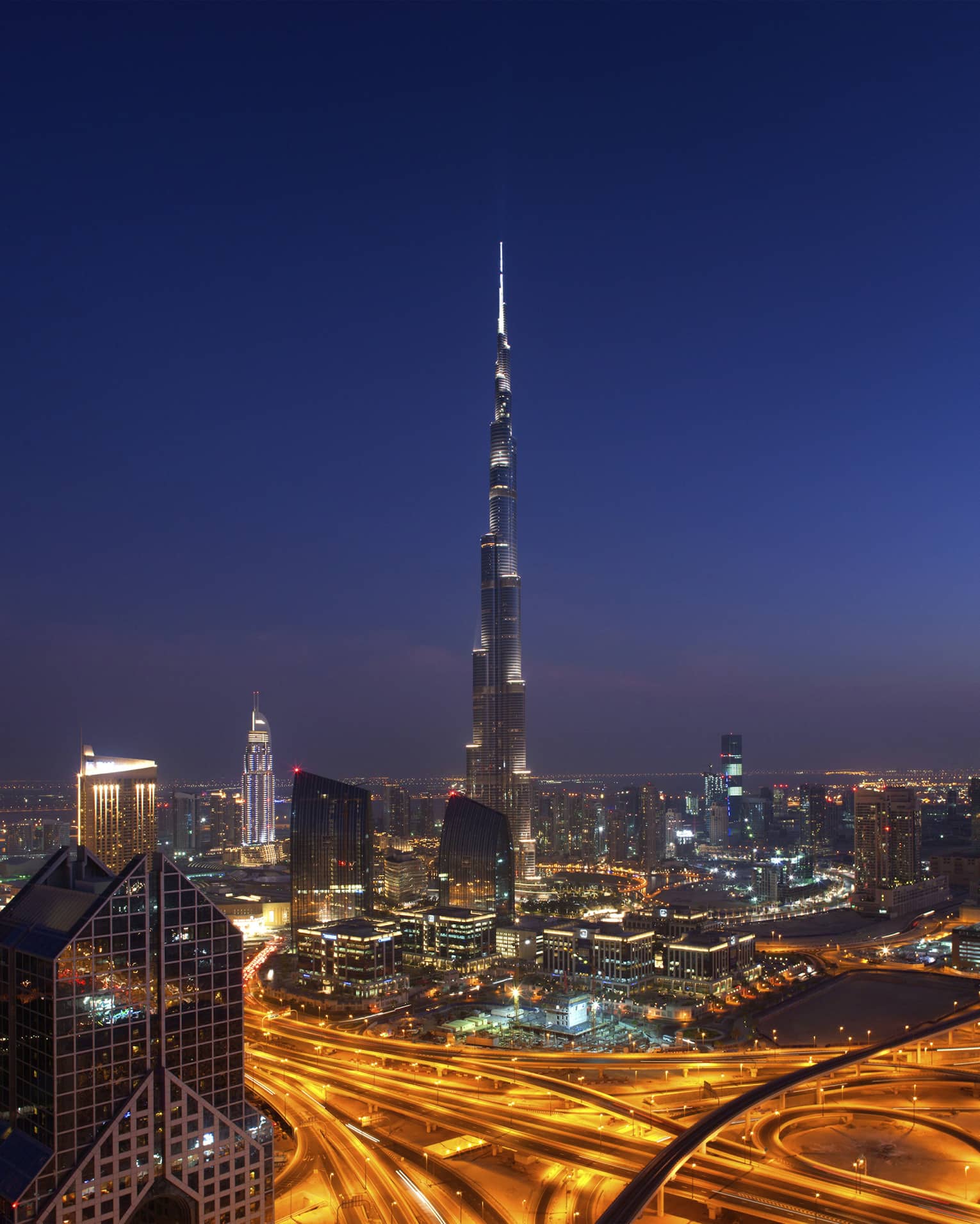 The Burj Khalifa towering over downtown Dubai under a dark starless sky, the city lit by the glow of cars and buildings.