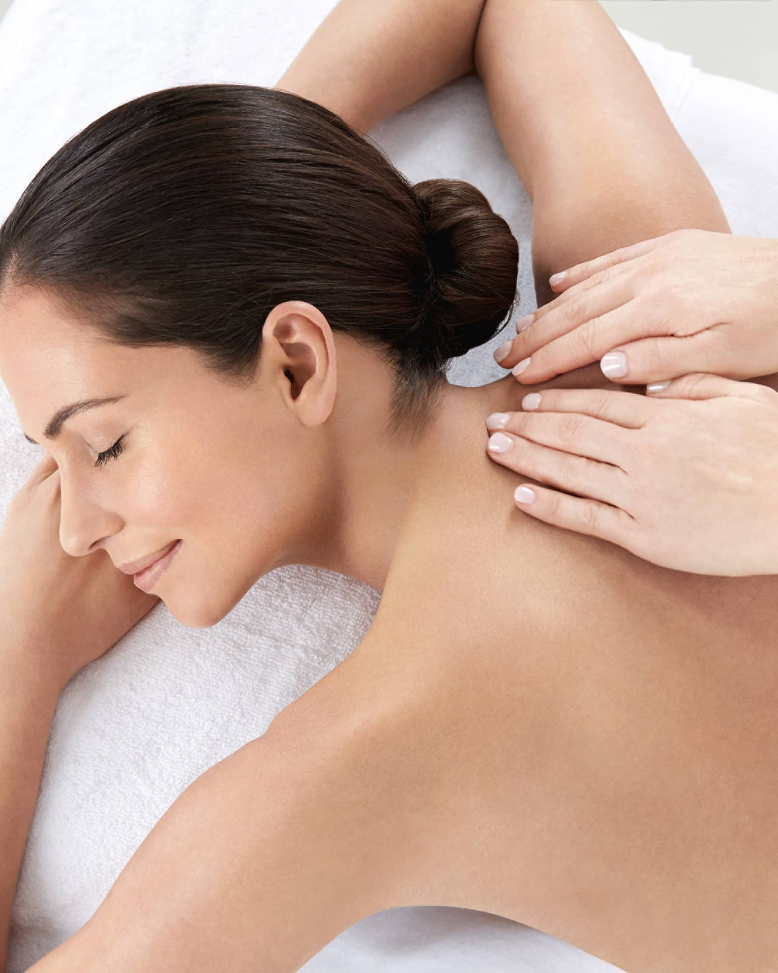 Woman smiles, lies on massage table as hands massage bare shoulders