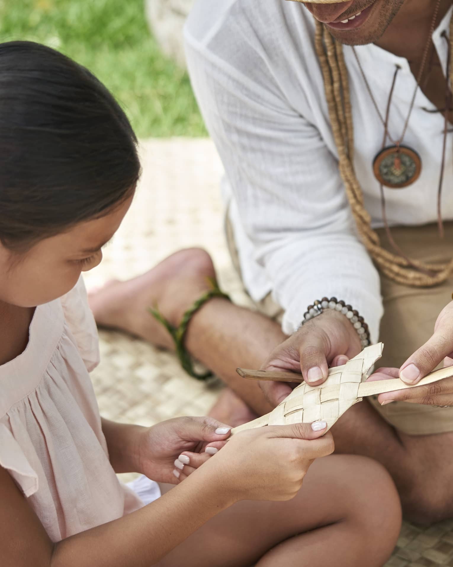 An adult shows a young girl how to weave a basket