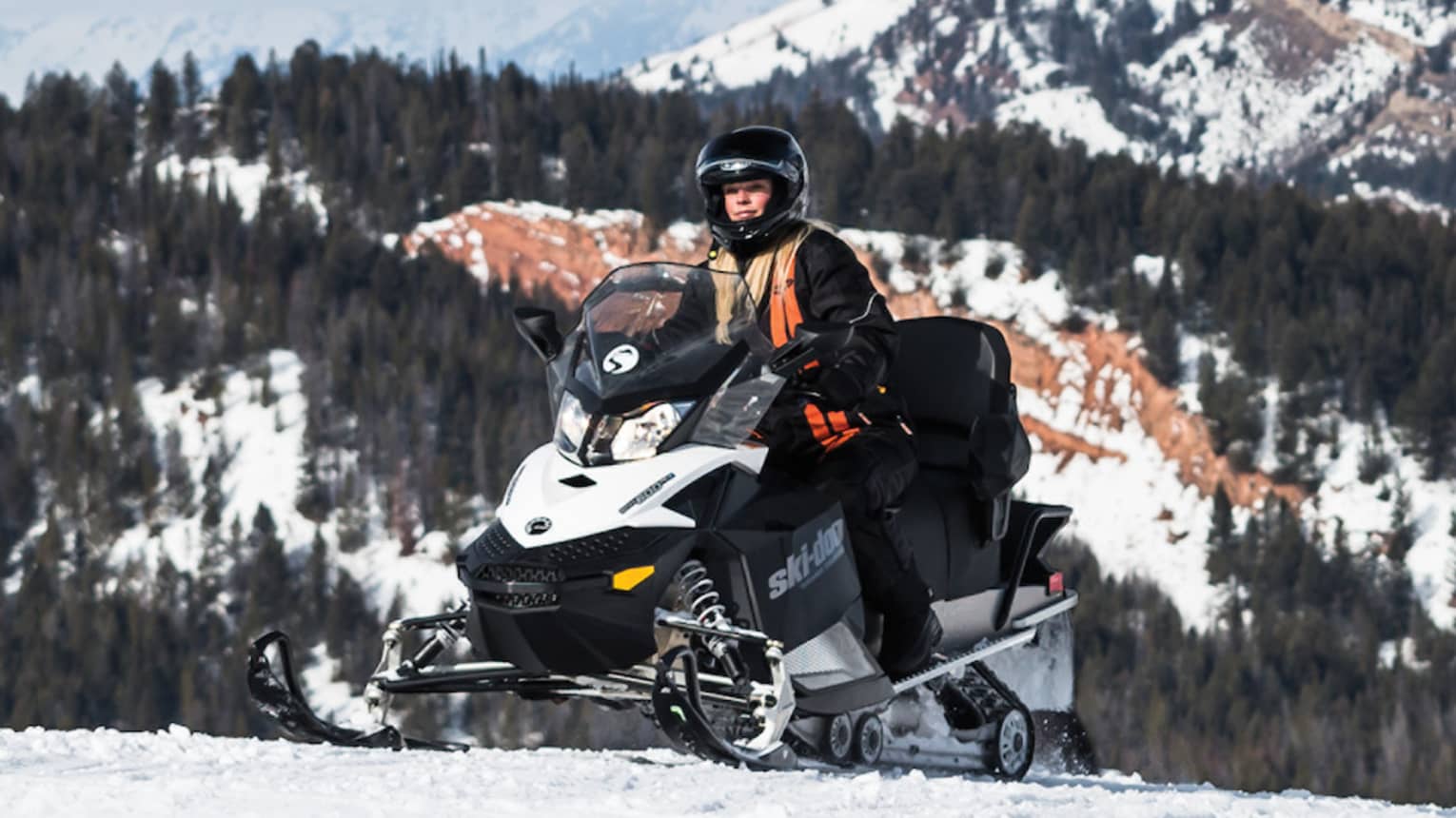 Person in snow gear on snowmobile with snowy mountain in backdrop
