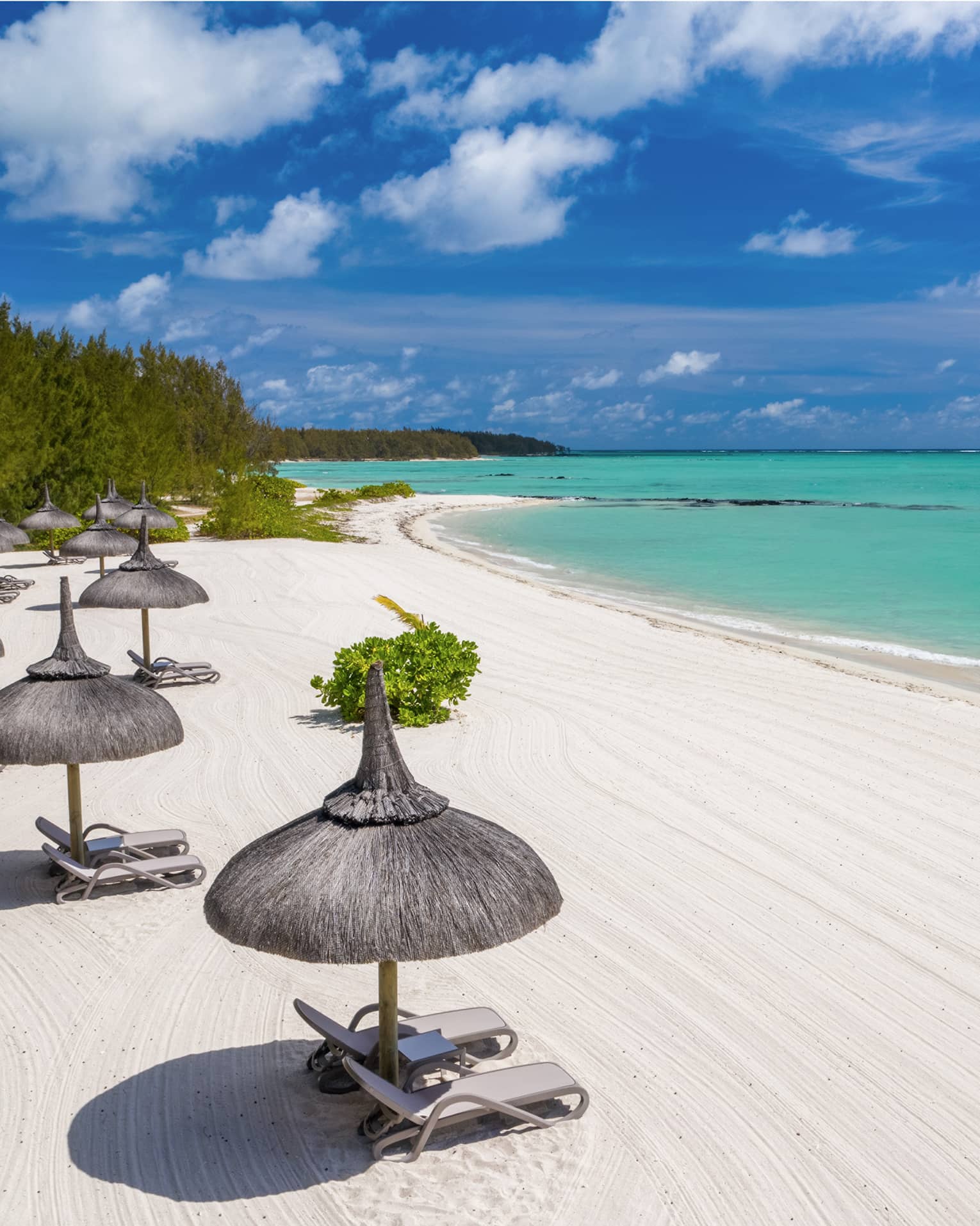 White sand beach with thatched umbrellas and lounge chairs and aqua ocean with blue sky above