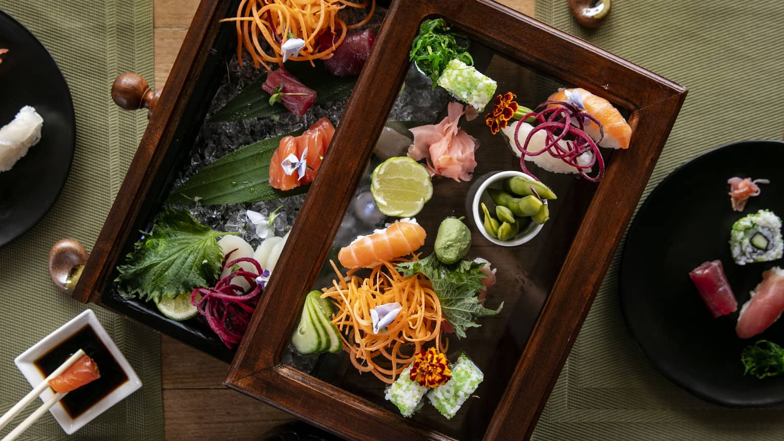 Aerial view of two people holding chopsticks eating sushi beautifully presented in Bento box