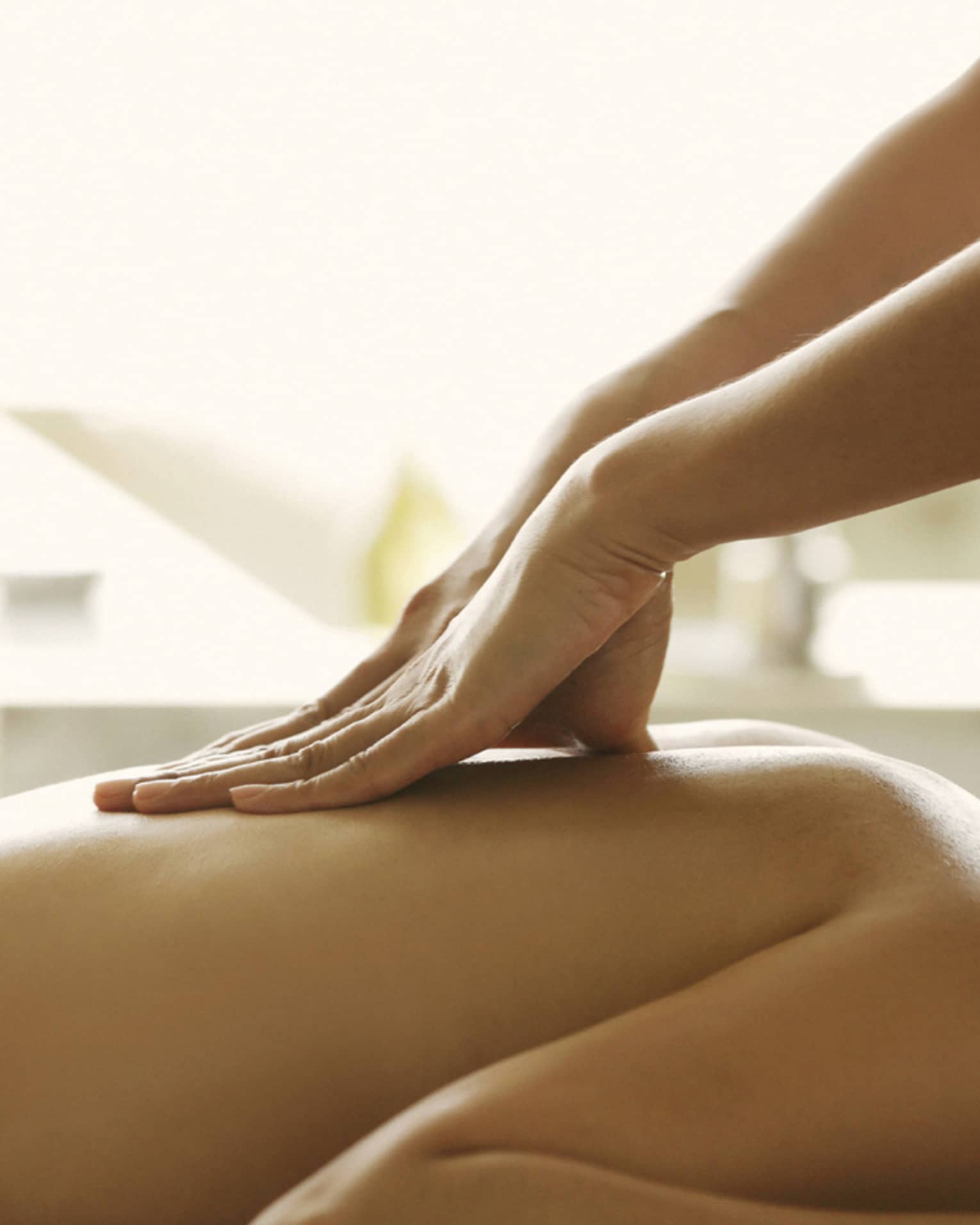 Masseuse reaches over, massages woman's bare back as she lies on spa table