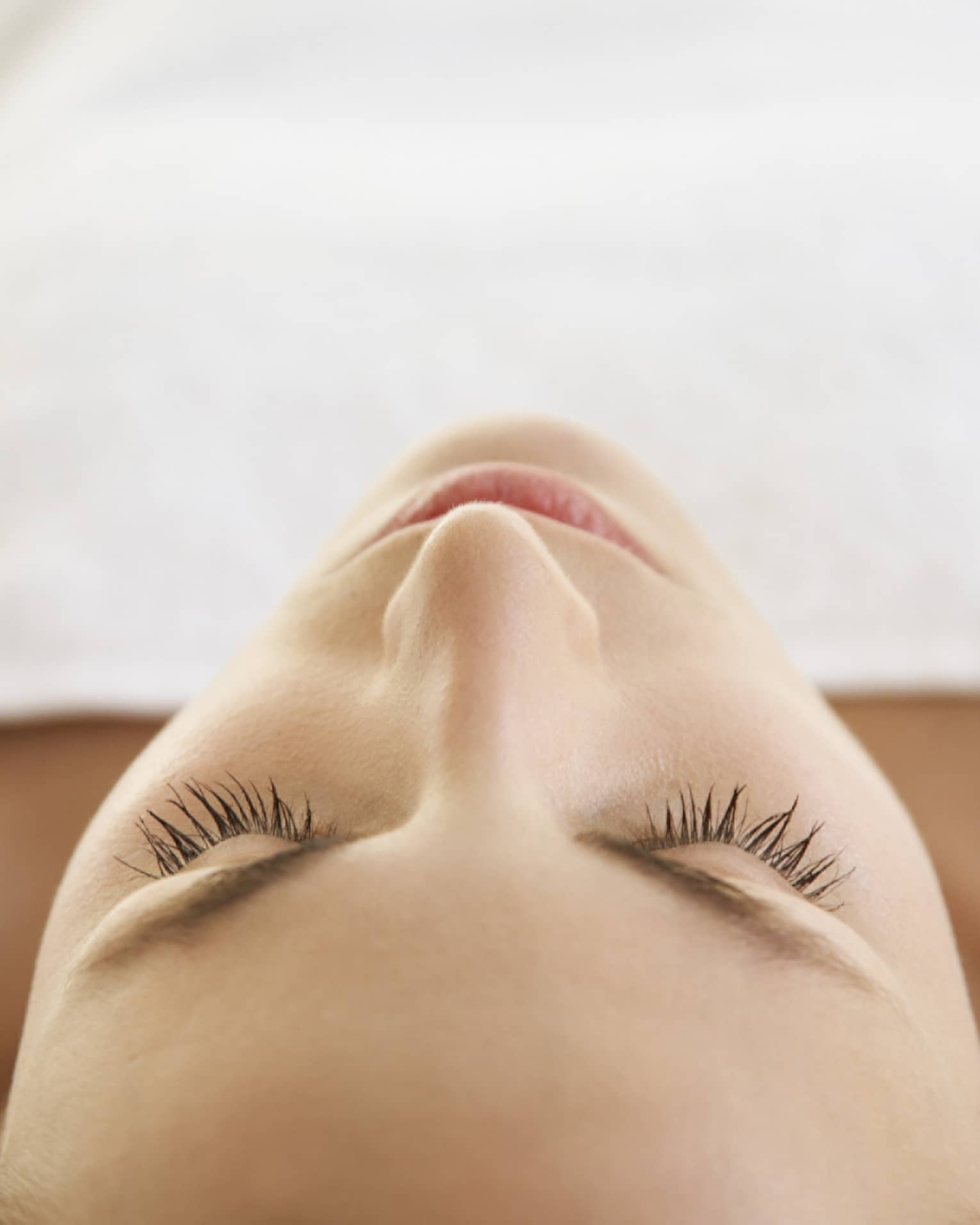 Woman lying down with eyes closed, bare shoulders, covered with white sheet