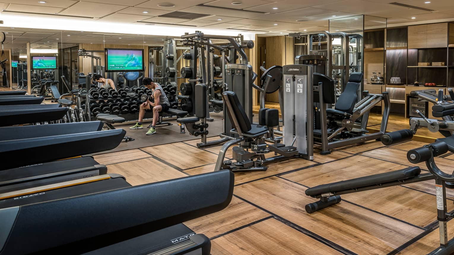 Man sits on bench, lifts weights on Fitness Centre by cardio machines 