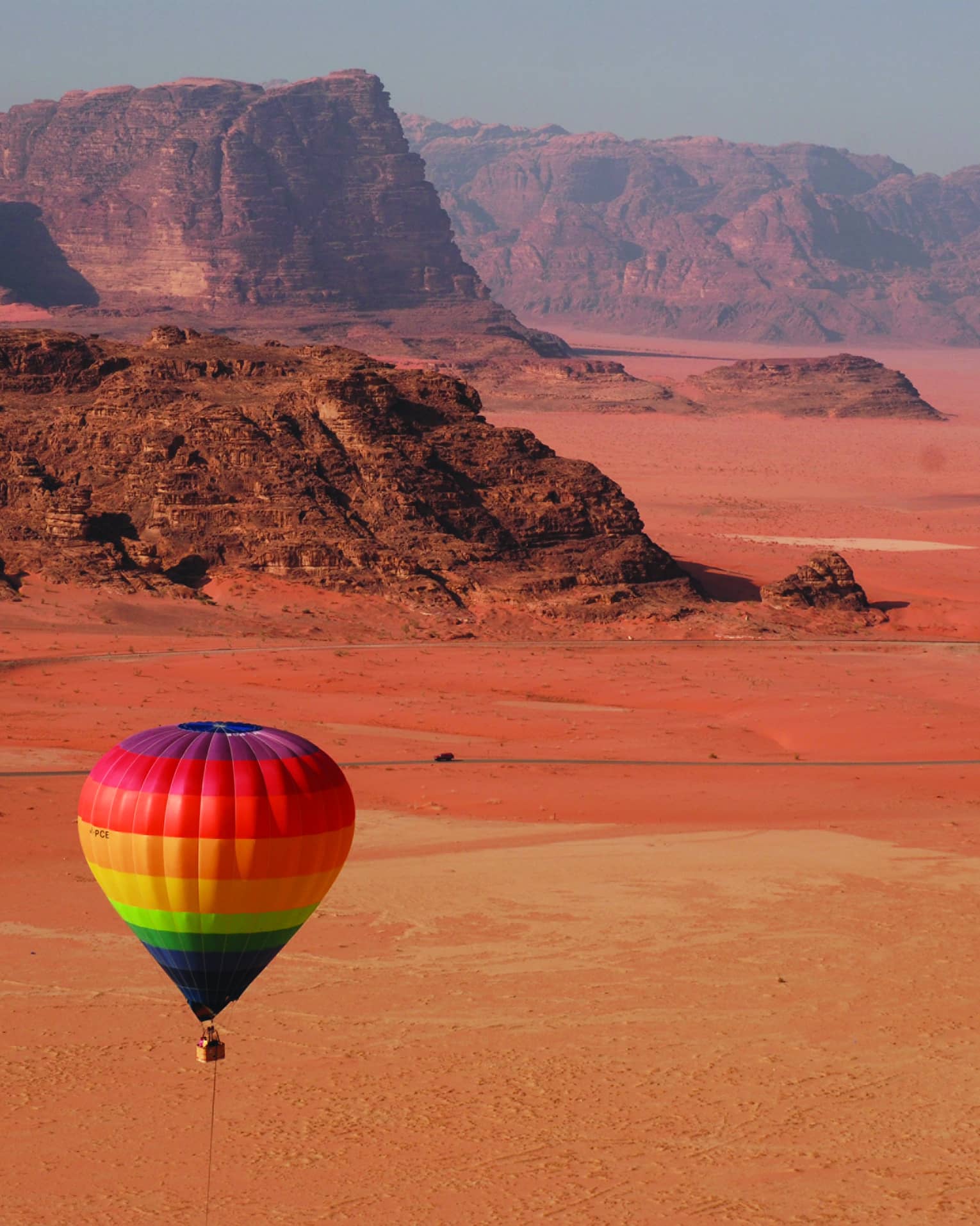 Rainbow hot air balloon flying over red sand in Jordan desert