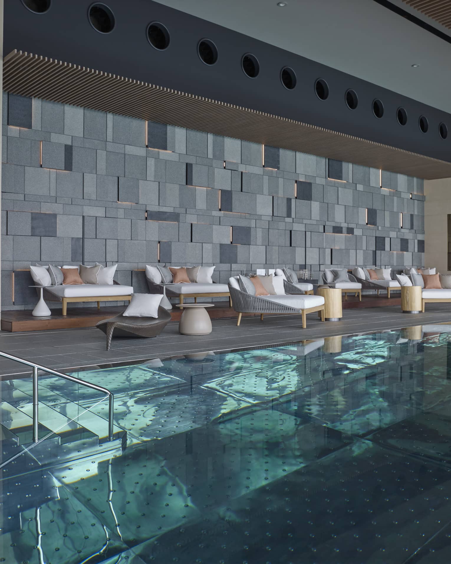 Indoor swimming pool, plush patio chairs on deck under modern brick wall