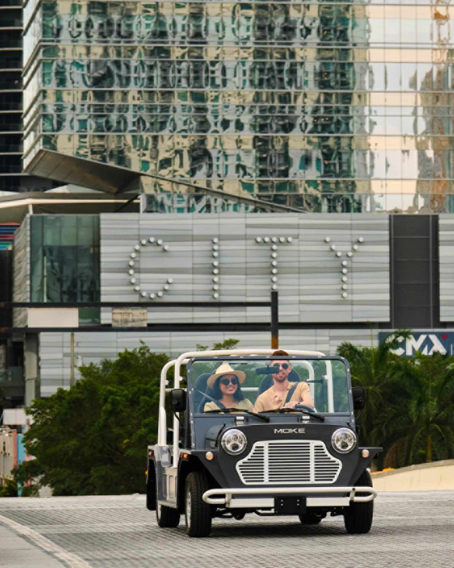 Two guests driving a car on the road with a building in the background.