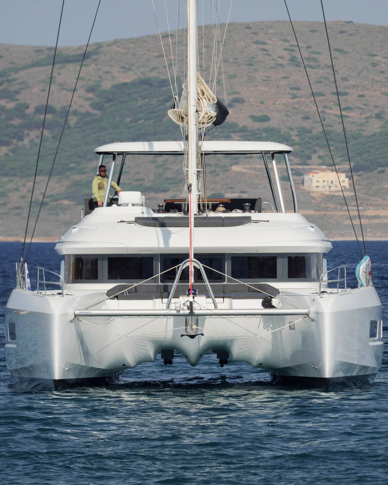 Stern view of luxury sailboat in blue water with captain at helm
