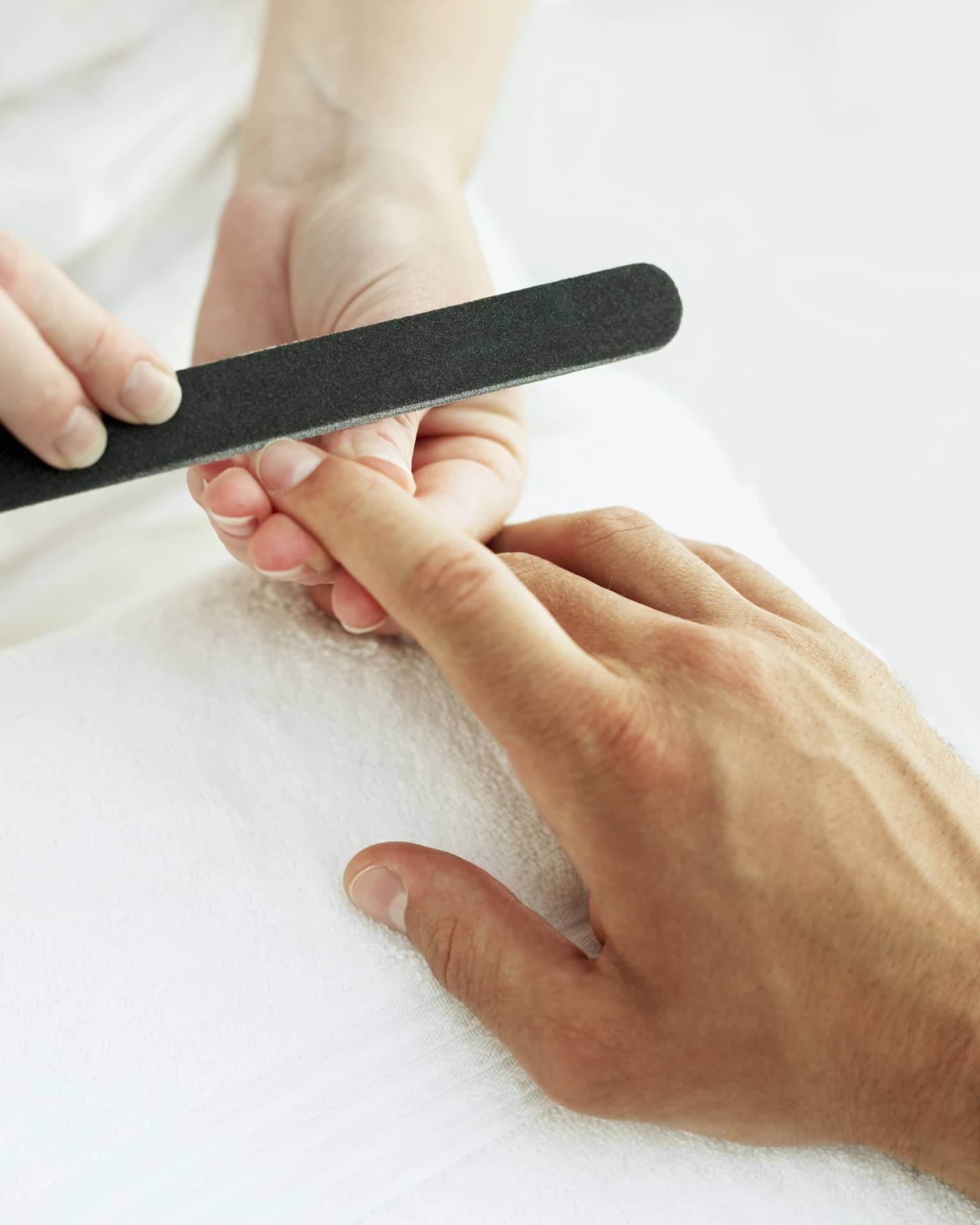 Woman holds manicure nail file to man's fingernails over white towel