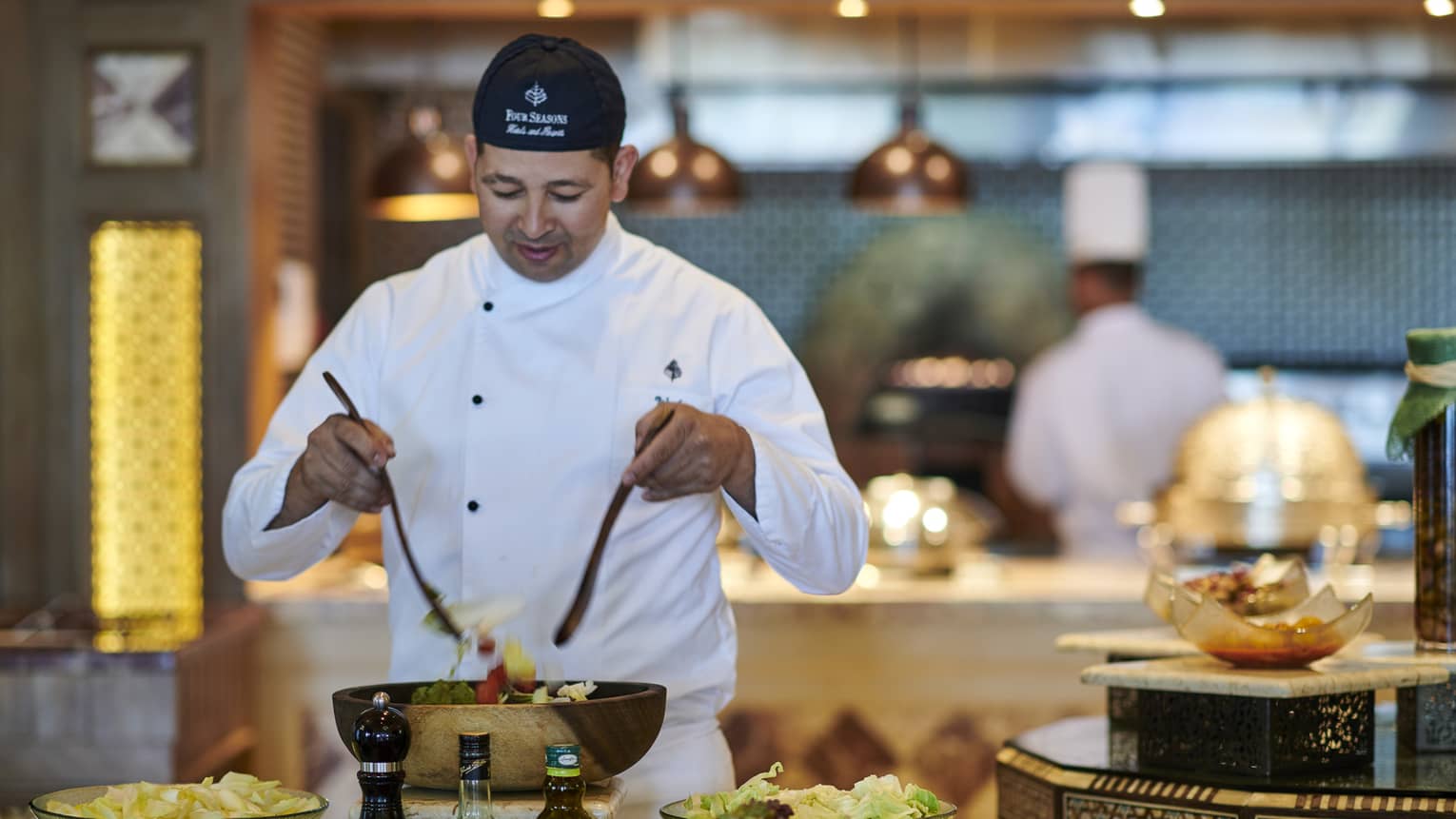 Chef tosses salad at buffet station with chopped vegetables in bowls
