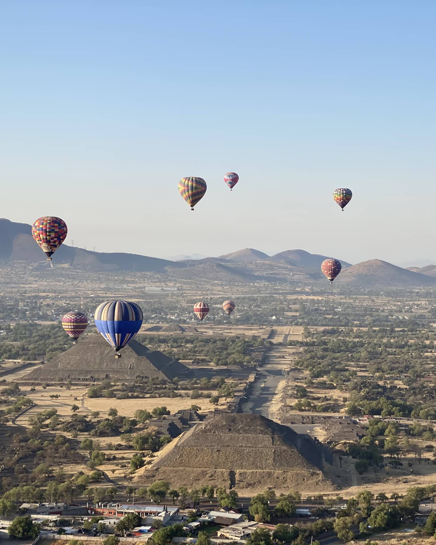 Hot-air balloons floating over old temples in a dessert covered in shrubs.