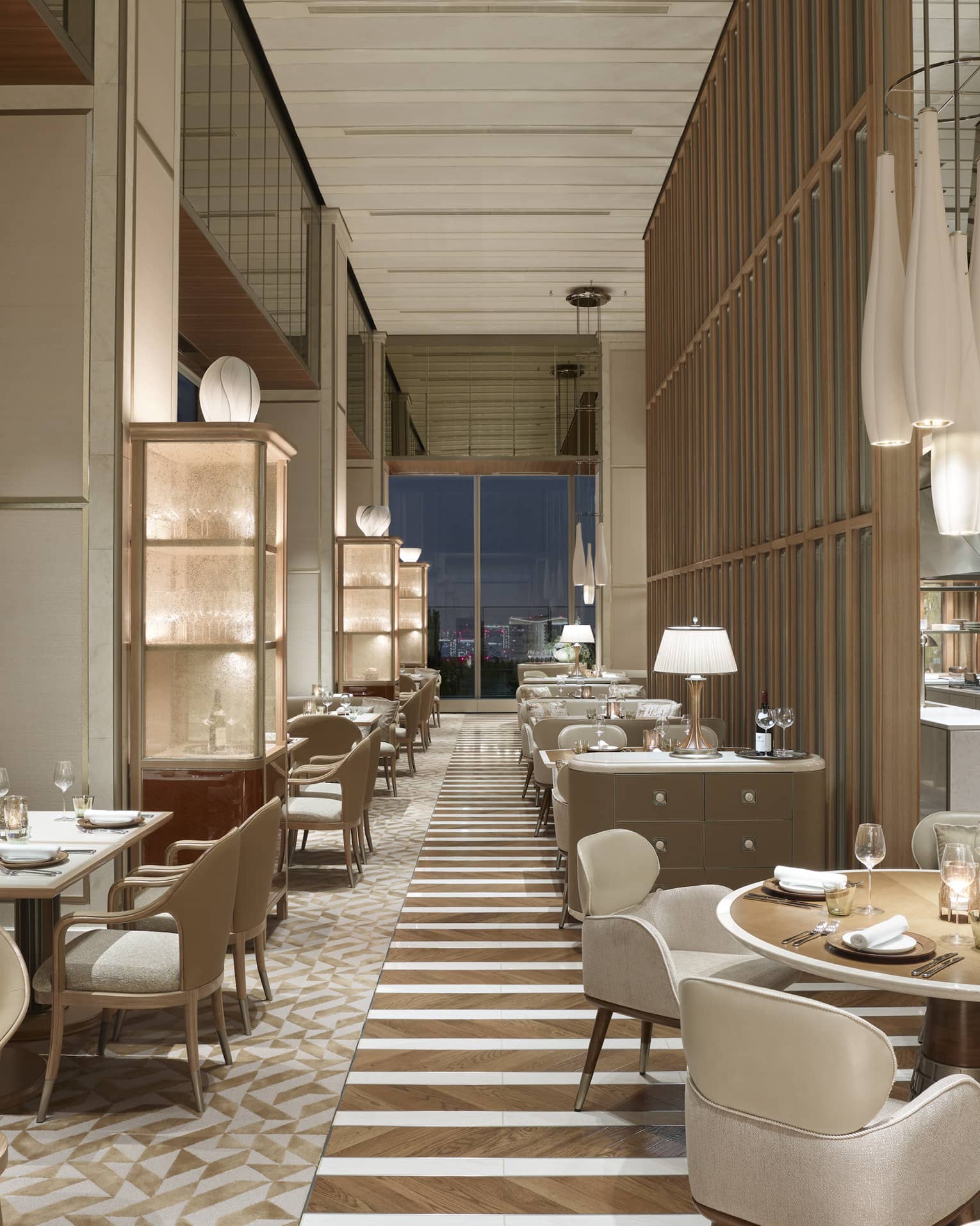 Restaurant with off-white chairs and sofas, elegant chandeliers, windows with nighttime views