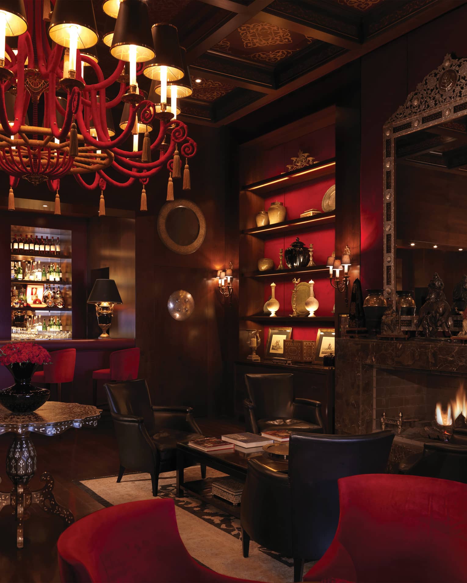 Bar interior with dark wood, red chandelier, shelf and velvet bar stools, arabesque ceiling, fireplace