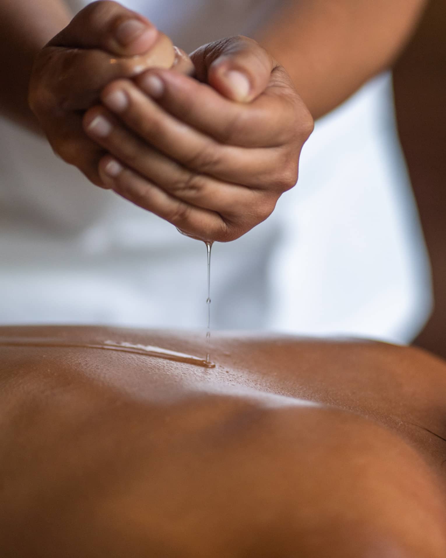 Delicate hands apply oil to a guest's back during a spa treatment