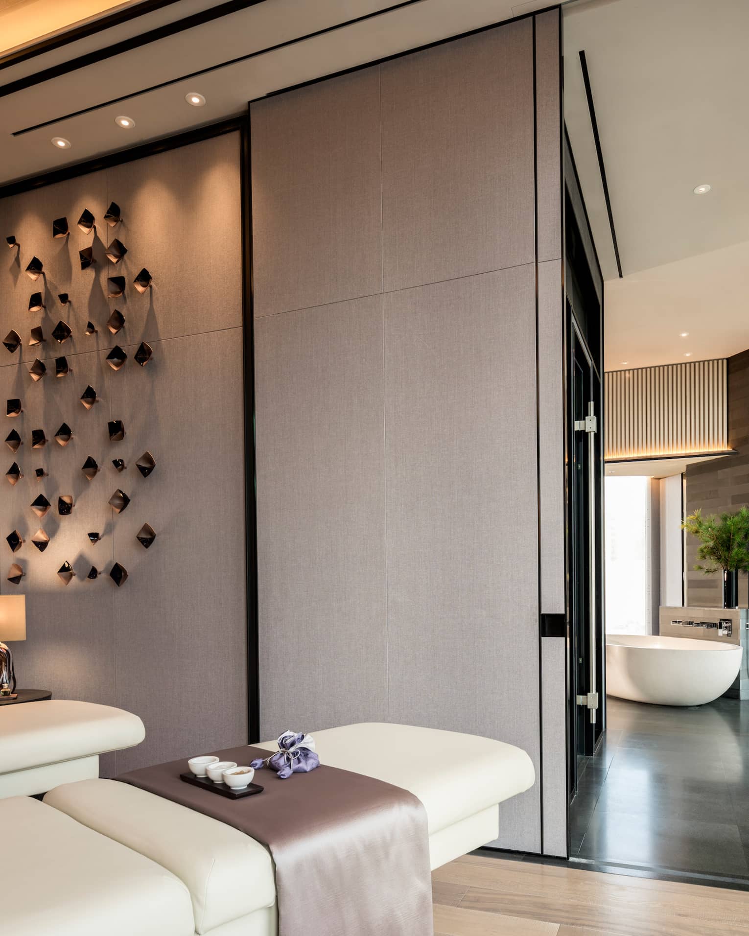 Couples massage beds under modern wall sculptures by hall leading to spa tub